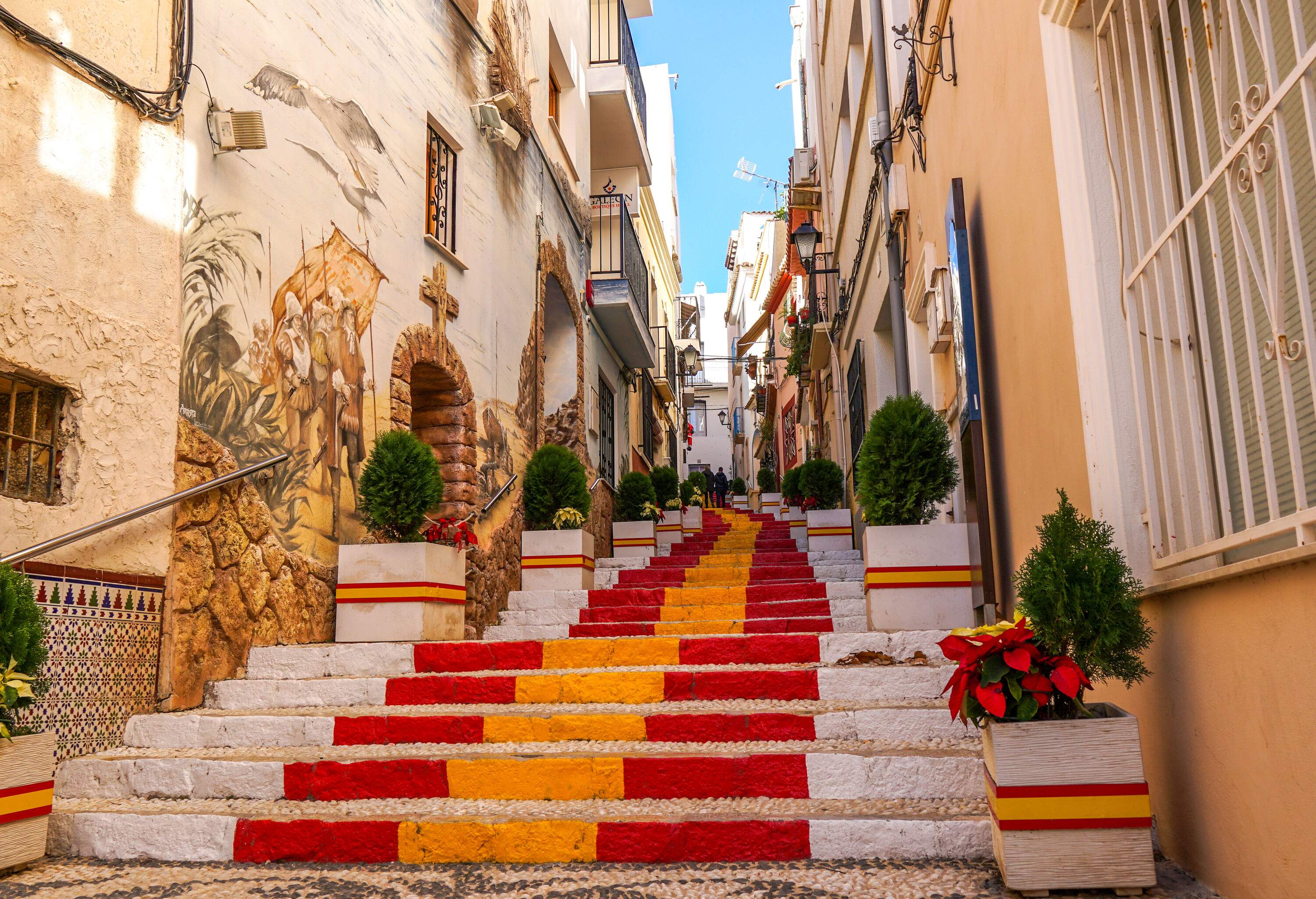 A stairway painted in red and yellow between buildings with paintings on the walls.