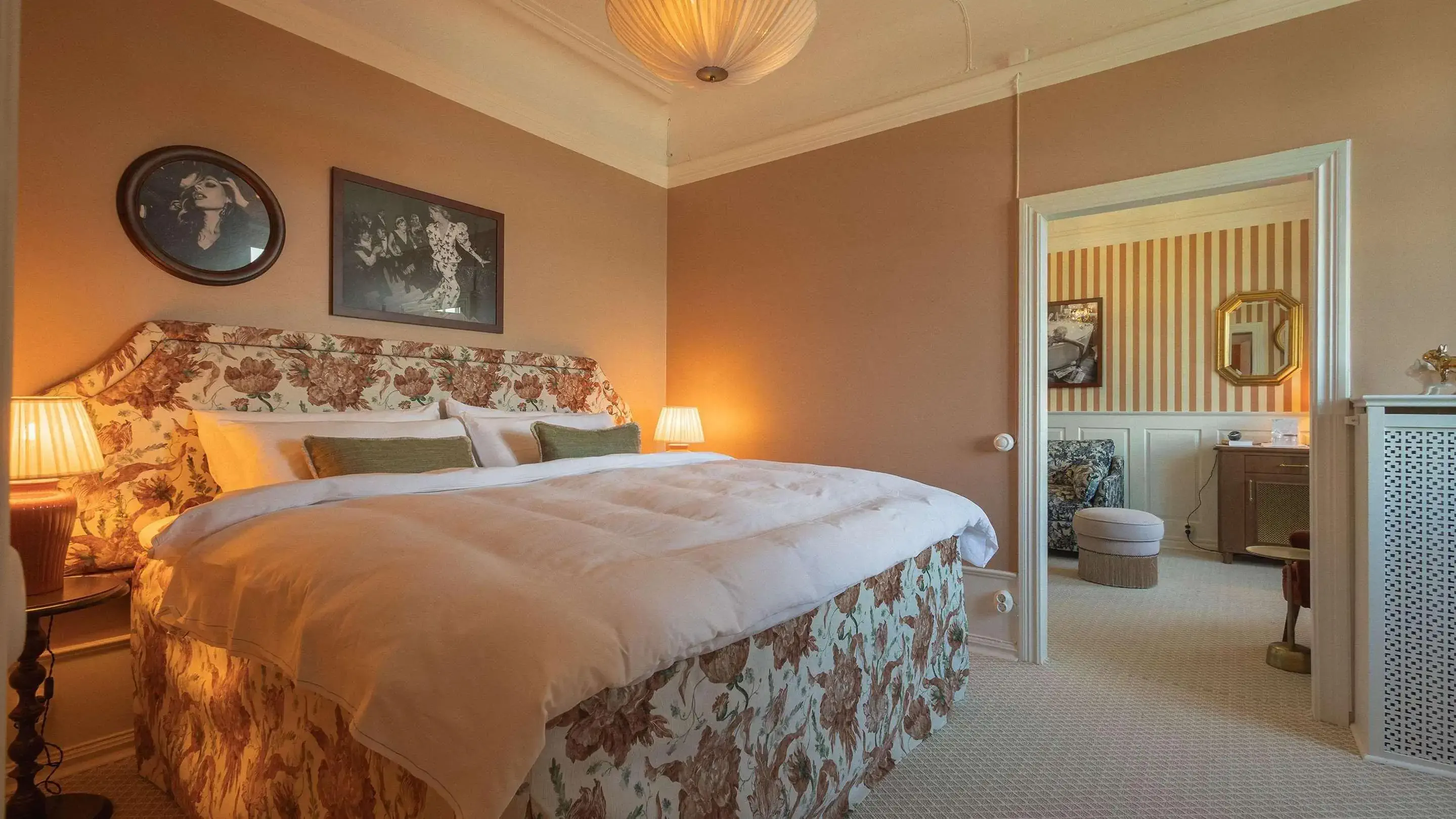 a cosy oldschool hotel room with a big flower bed and pictures on the wall