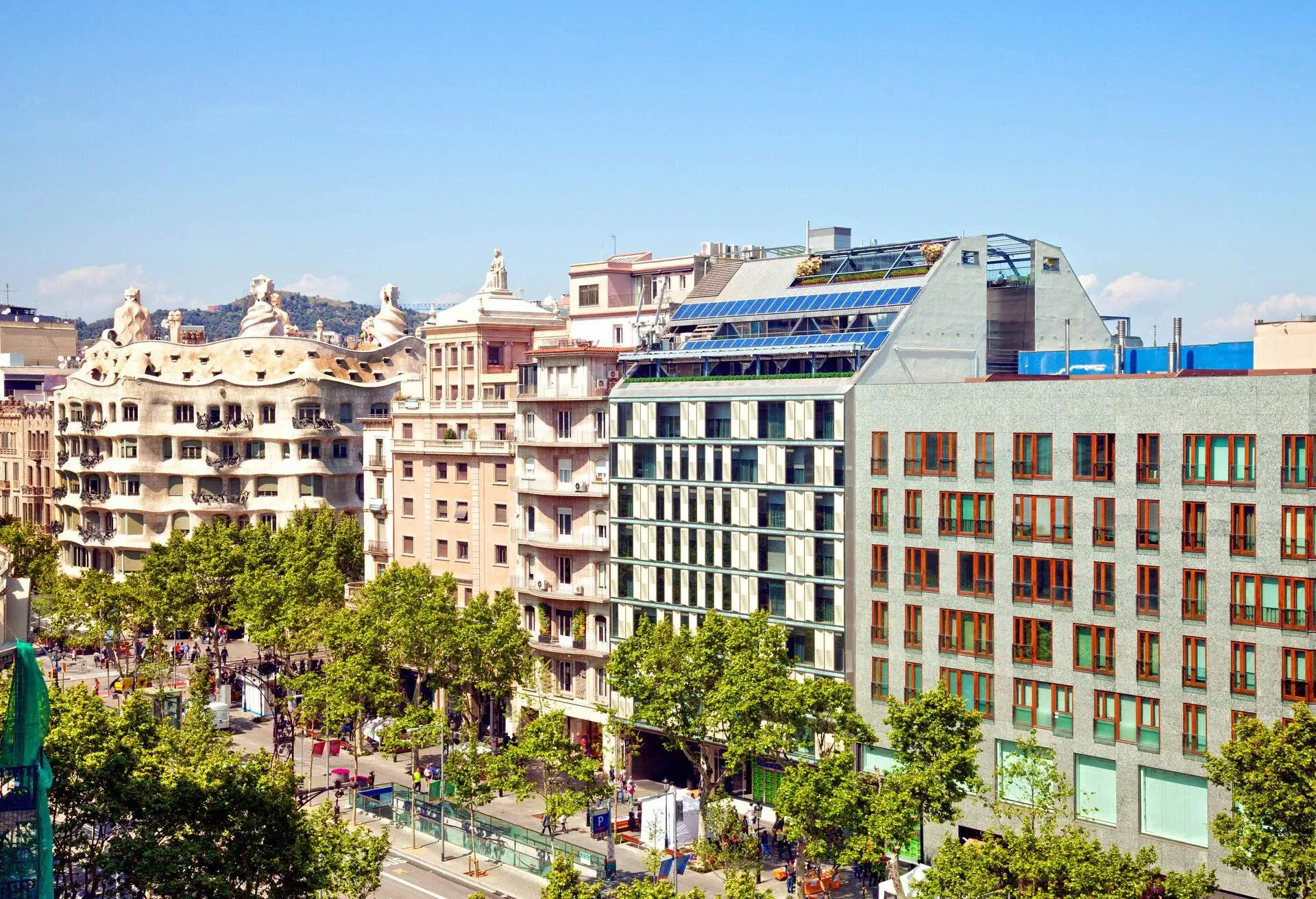 An avenue lined with trees on one side and eclectic buildings on the other.