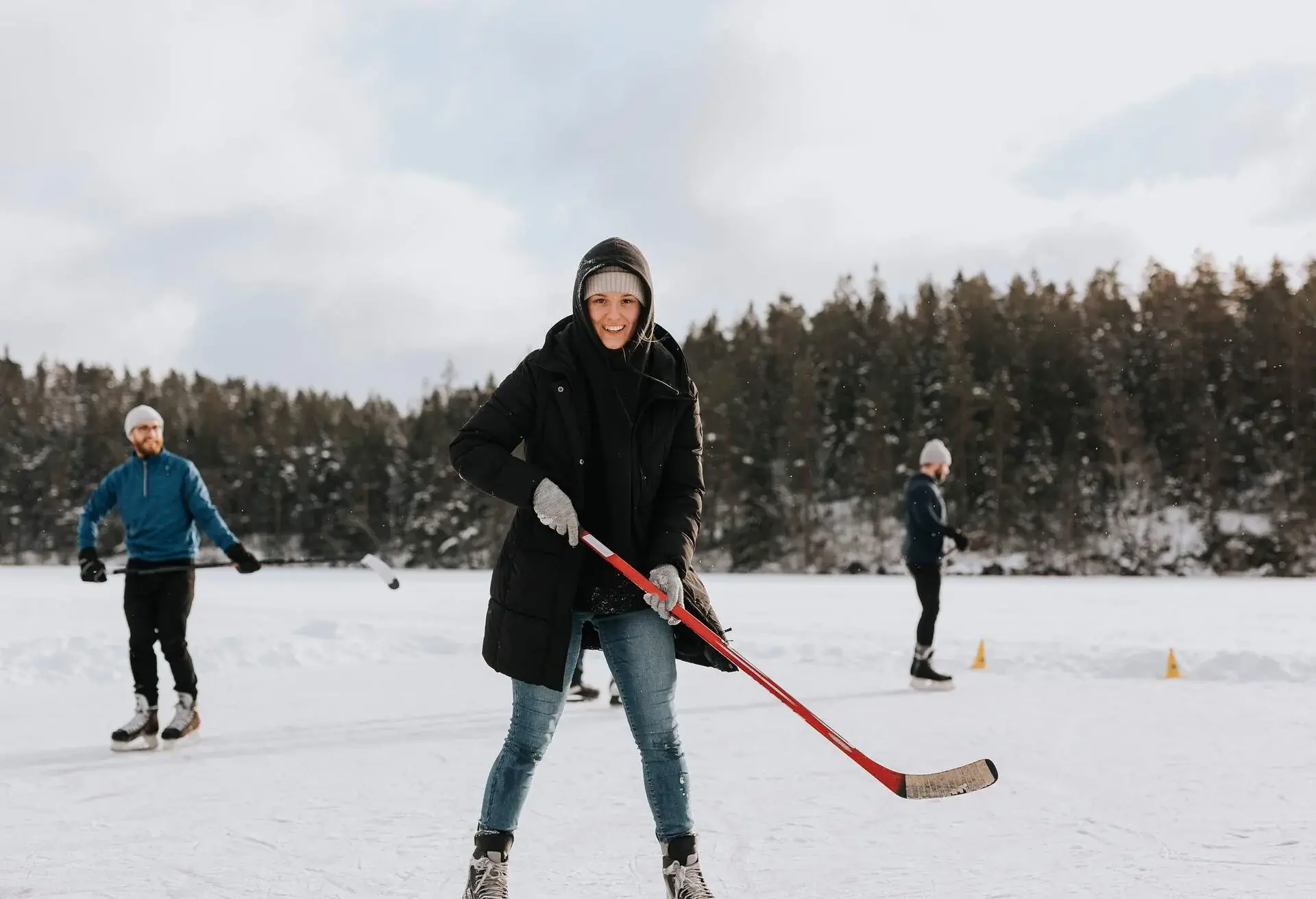 A woman playing ice hokey on a frozen lake with two people behind her