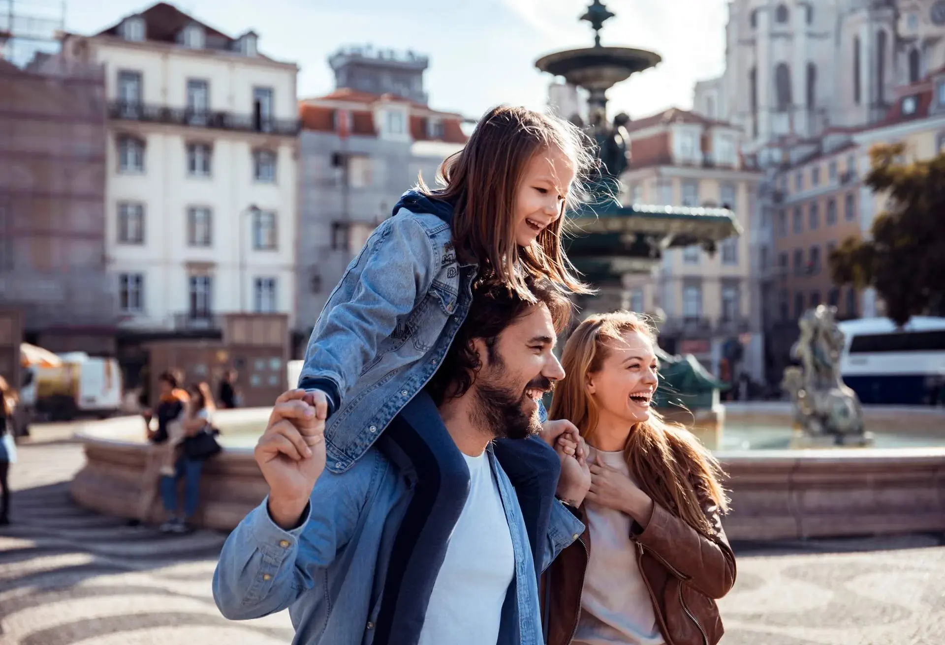 A young family of three strolling through a square past a huge water fountain.