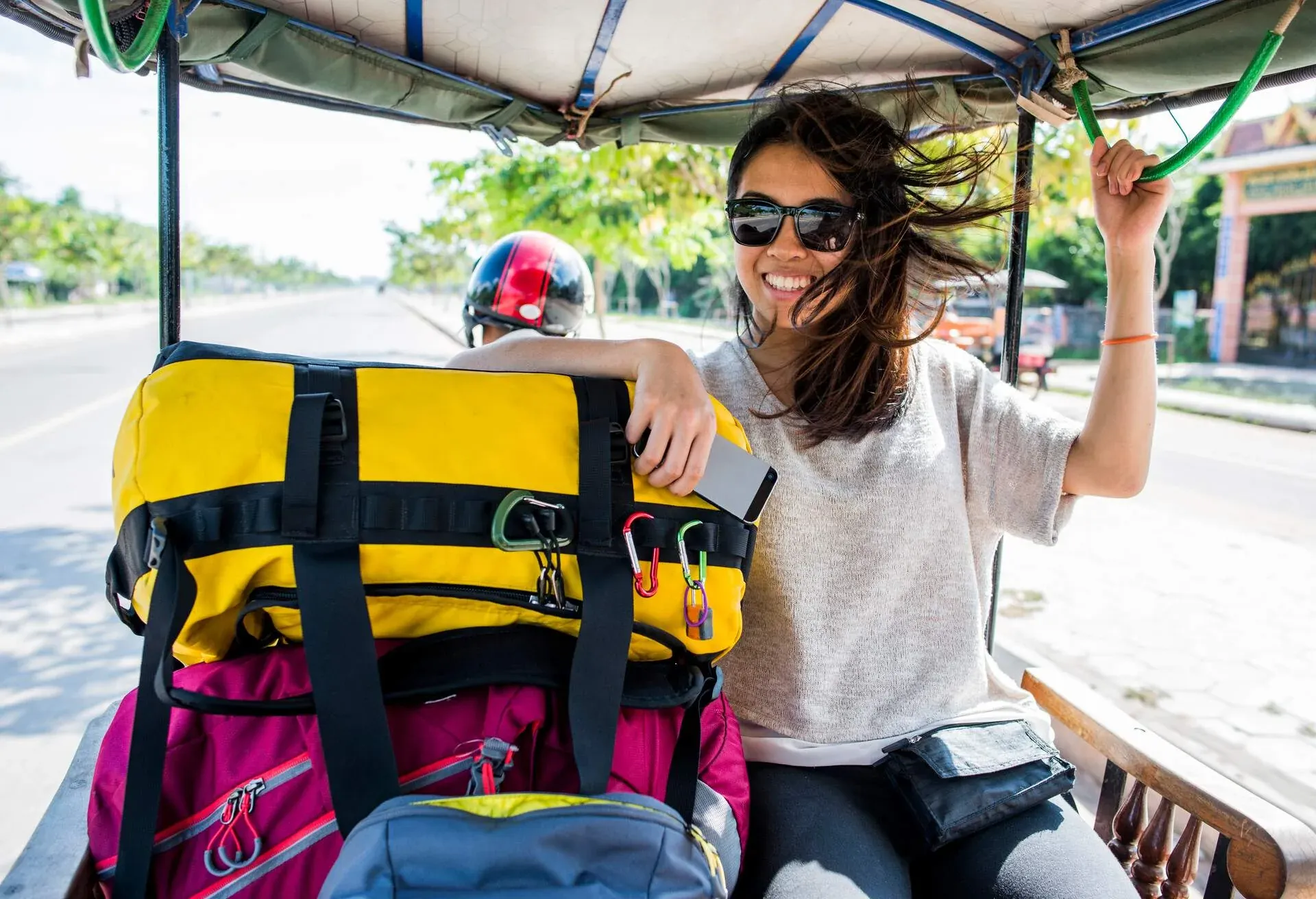 Female backpacker sitting on tuktuk with her luggage smiling at the camera