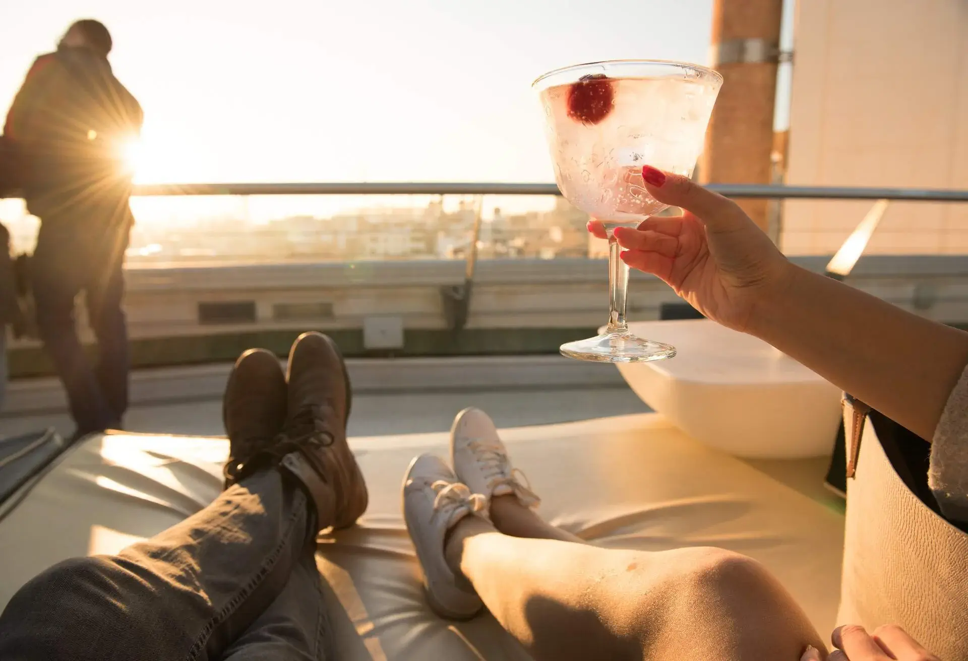 Girl raises cocktail glass to toast as she lies on the sofa of a rooftop bar  during sunset in Madrid, Spain