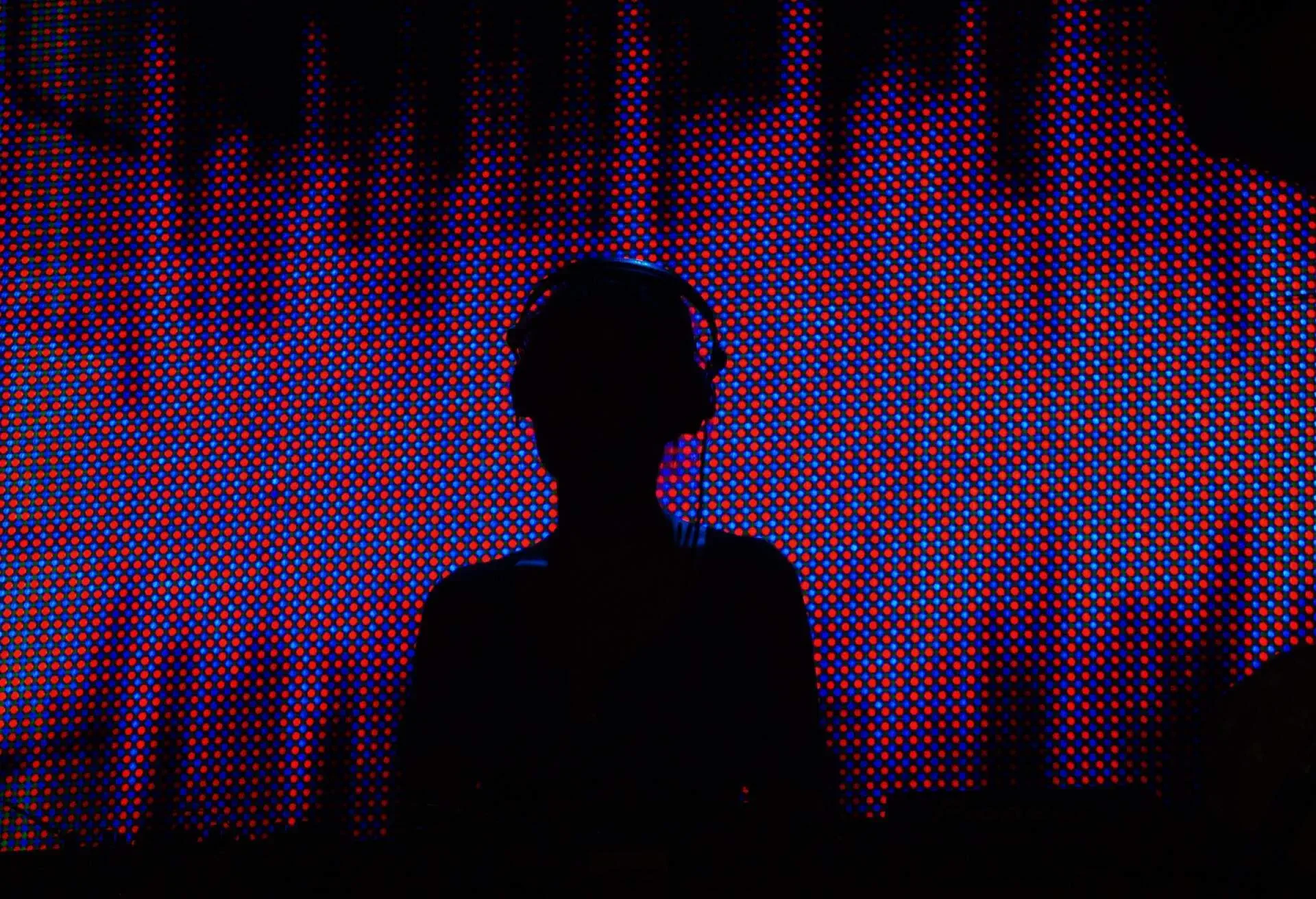 A DJ's silhouette against a neon background in a nightclub.