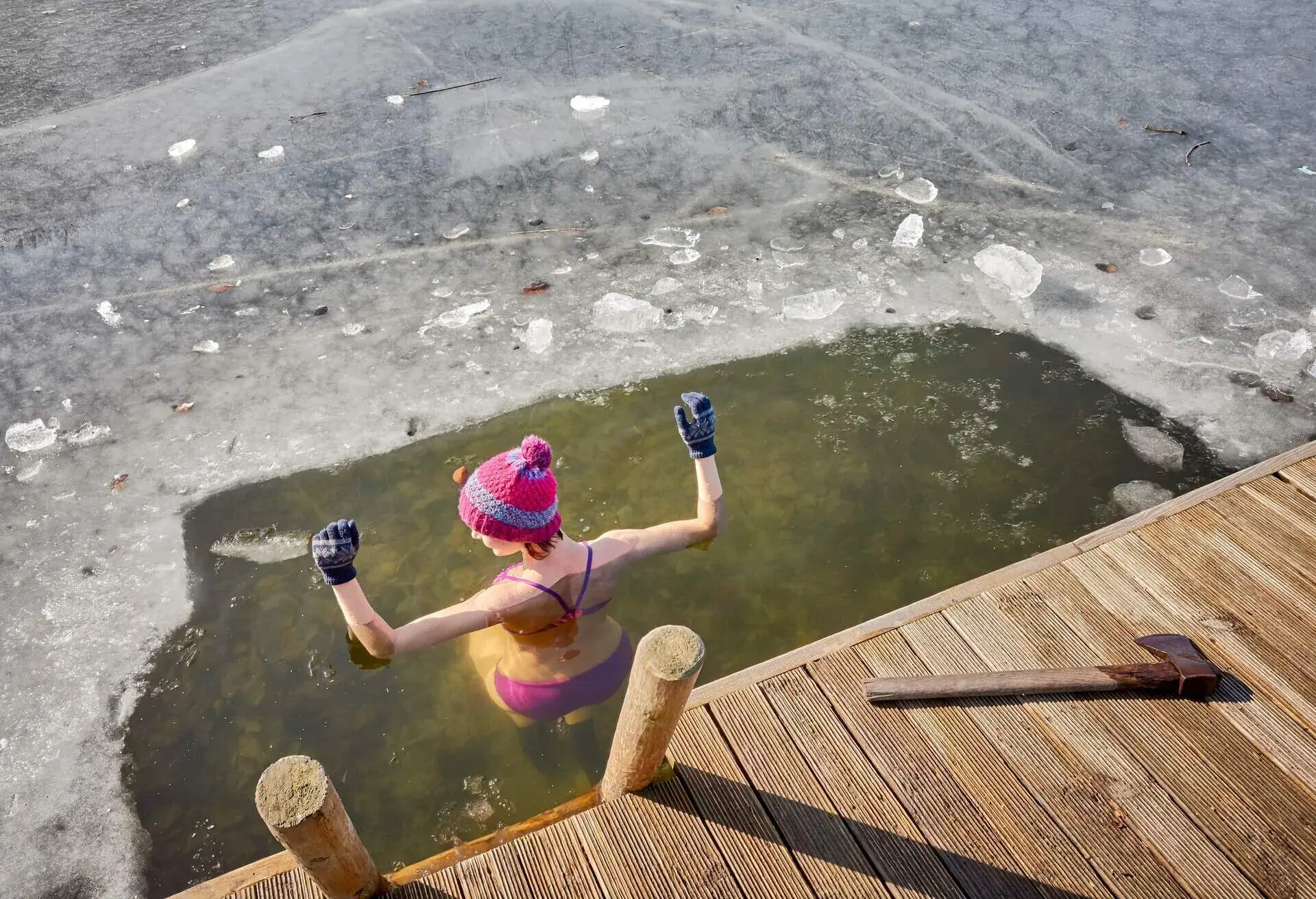 Woman wearing a wool hat and gloves dipping from a jetty into a hole carved with an axe into a frozen lake