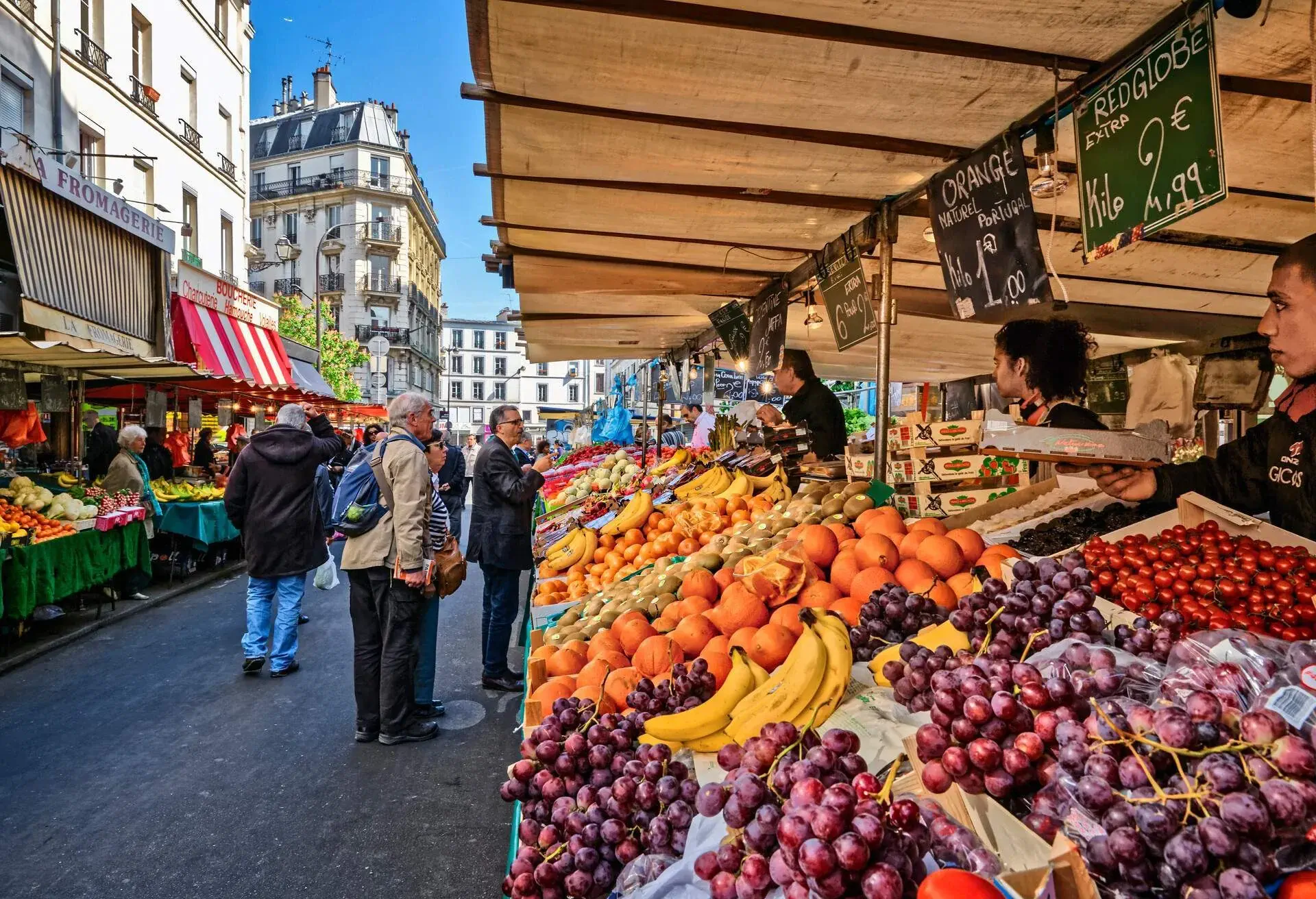 A greengrocer selling various fruits talking with customers.