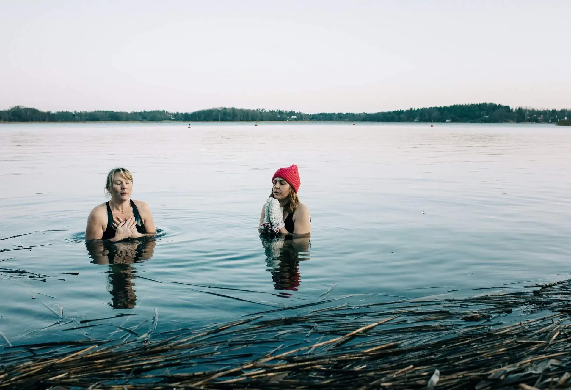 Two women with eyes closed dipping into the cold water of a lake on a winter day
