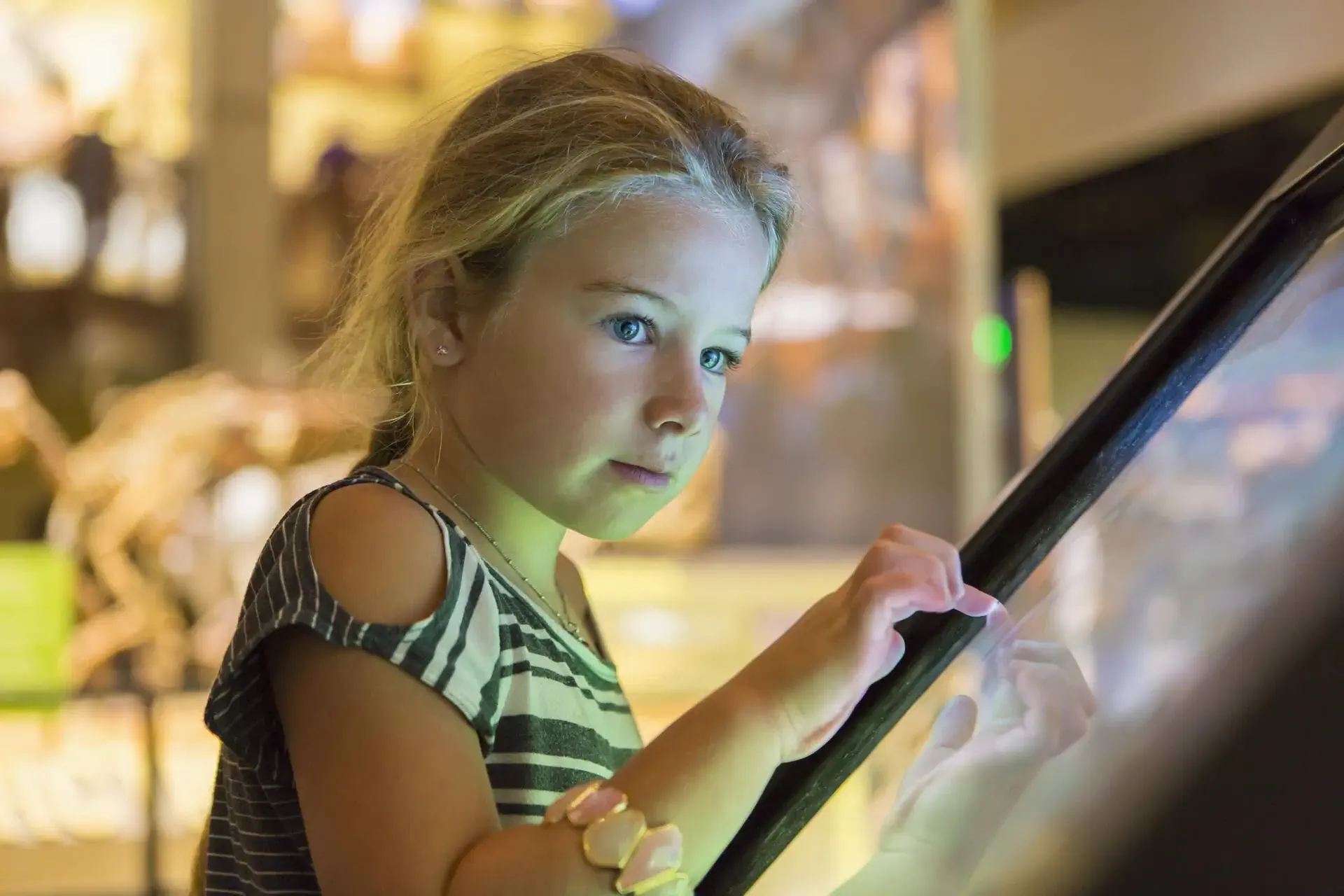 A young blonde girl using an interactive touchscreen device.