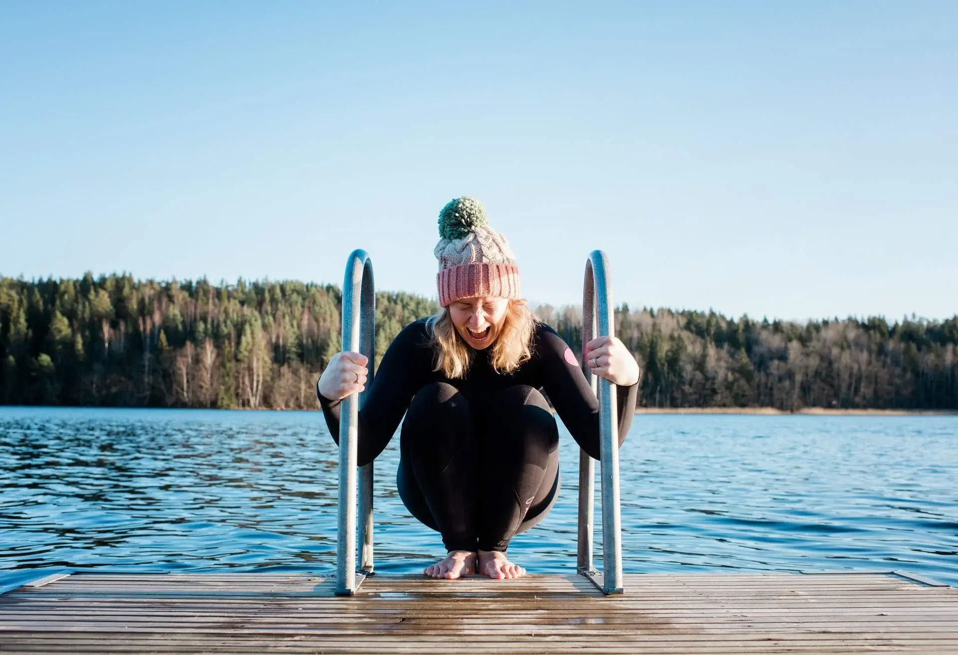 Woman wearing a wool hat and wetsuit concentrating before dipping in cold water on a lake ona sunny winter day