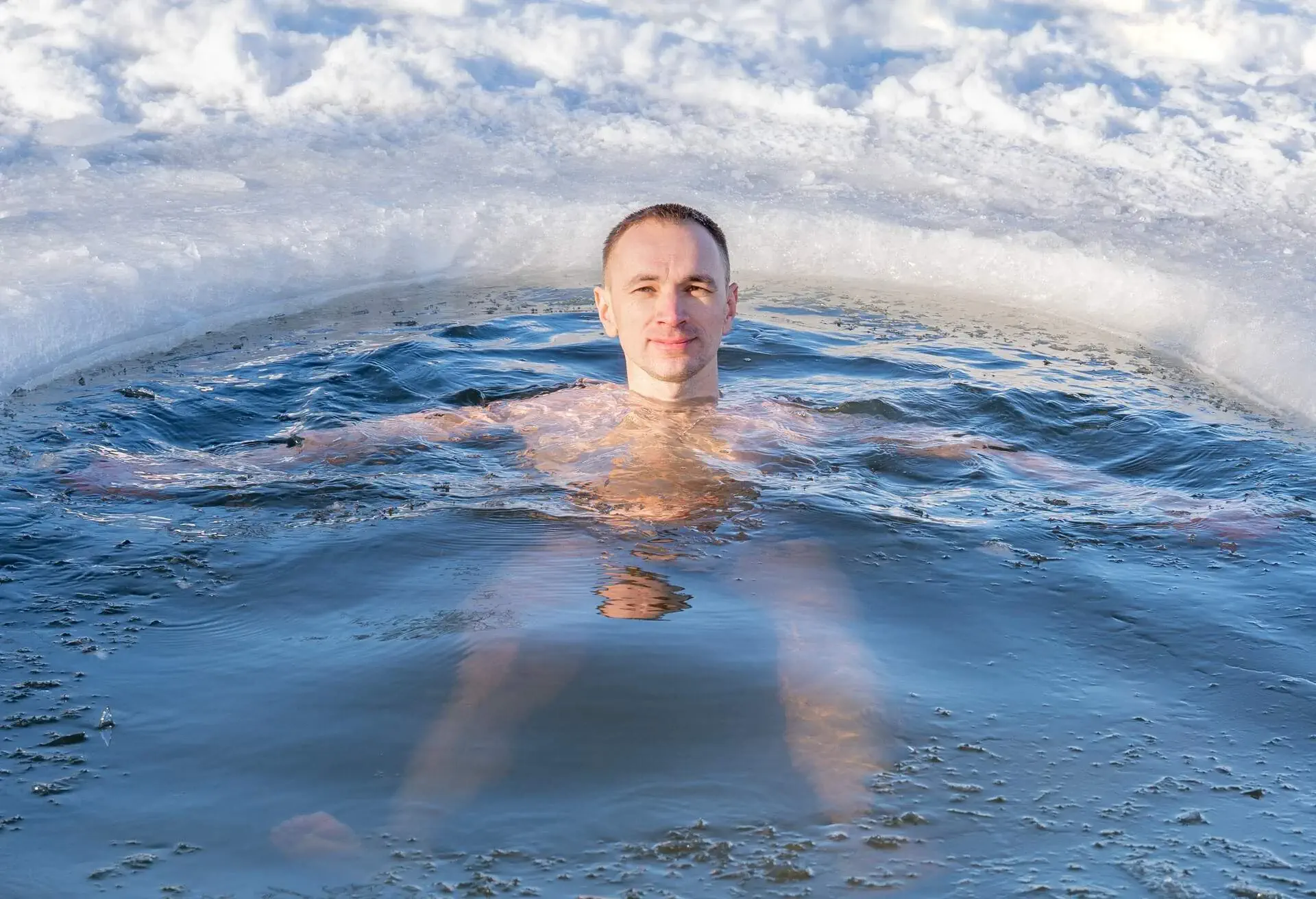 Man winter bathing into a hole on a frozen lake