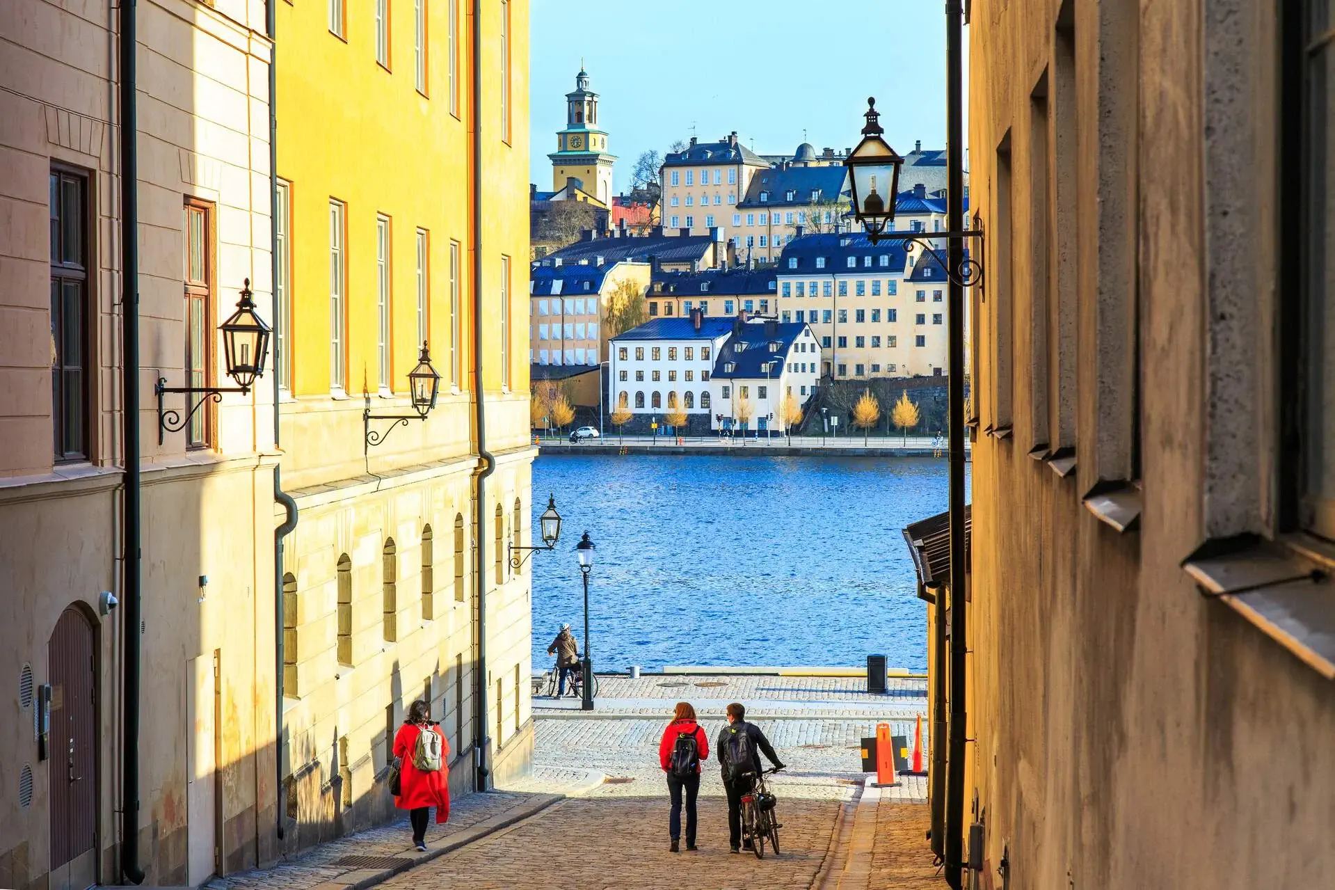 People on a cobbled street with a view of classic and elegant buildings across the waters.