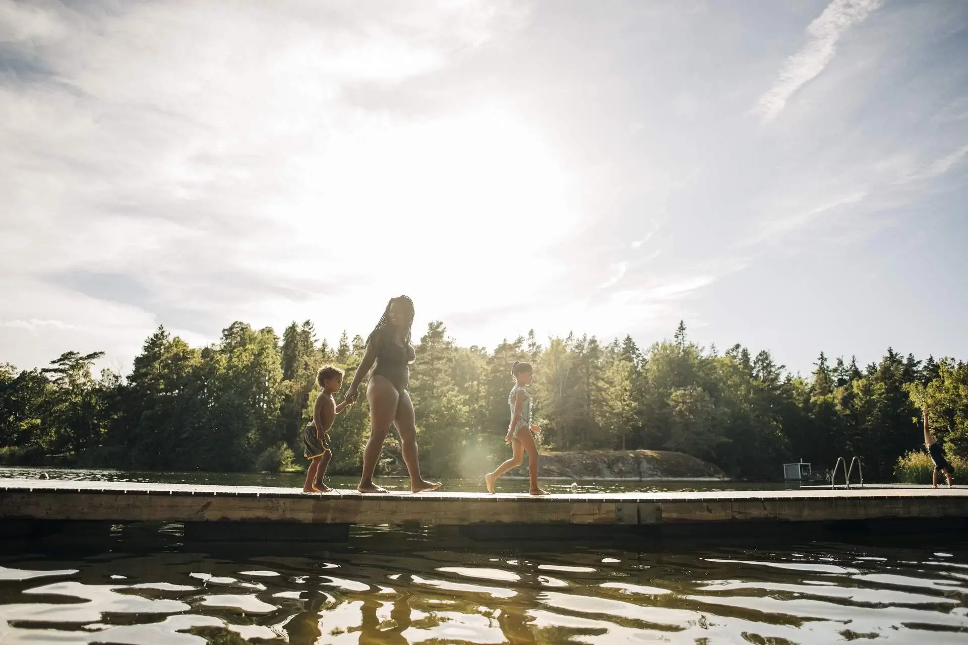 A woman and two children strolling on a boardwalk over a lake.