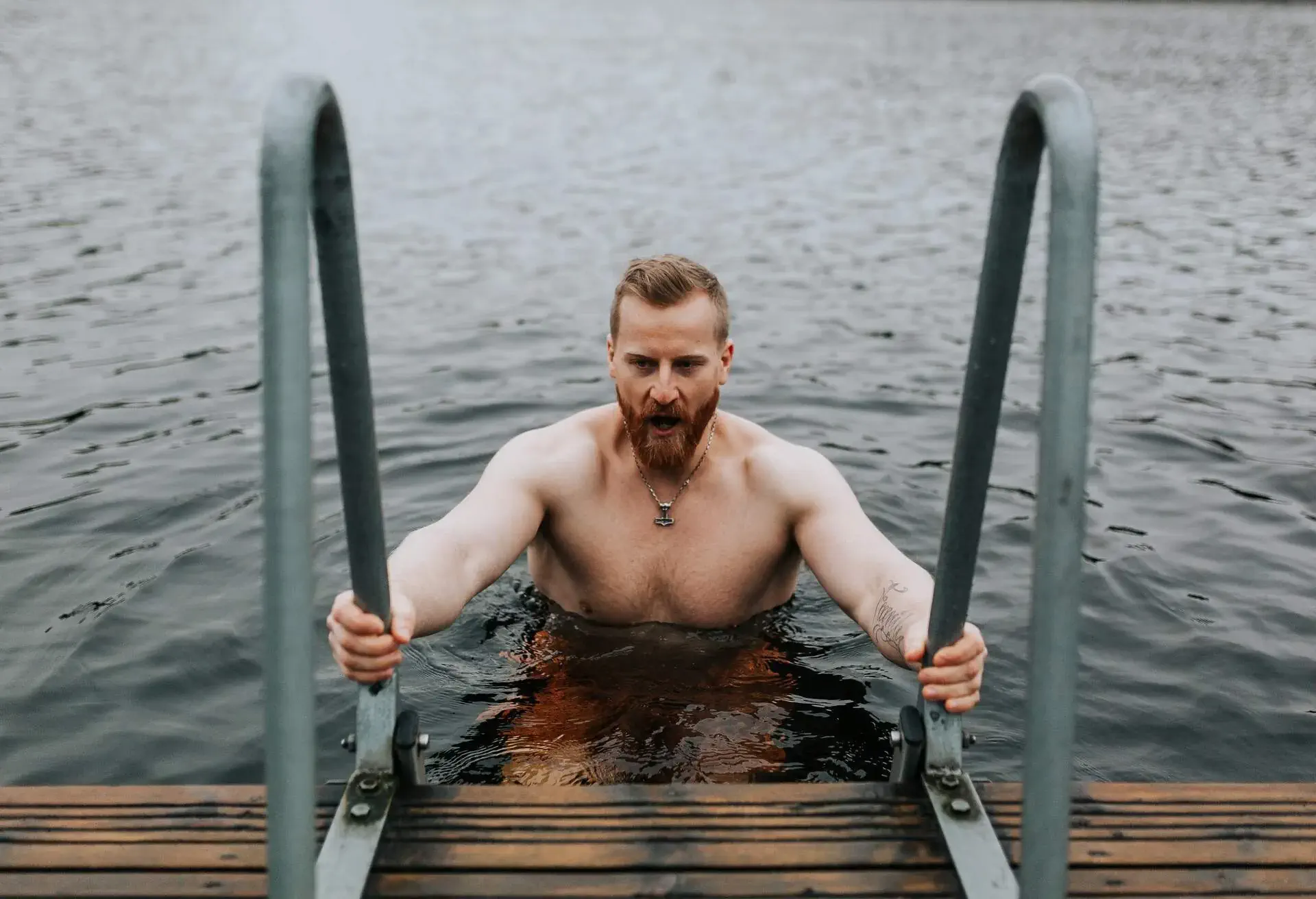 Bearded ginger man dipping into ice cold water from a jette during a winter swimming session