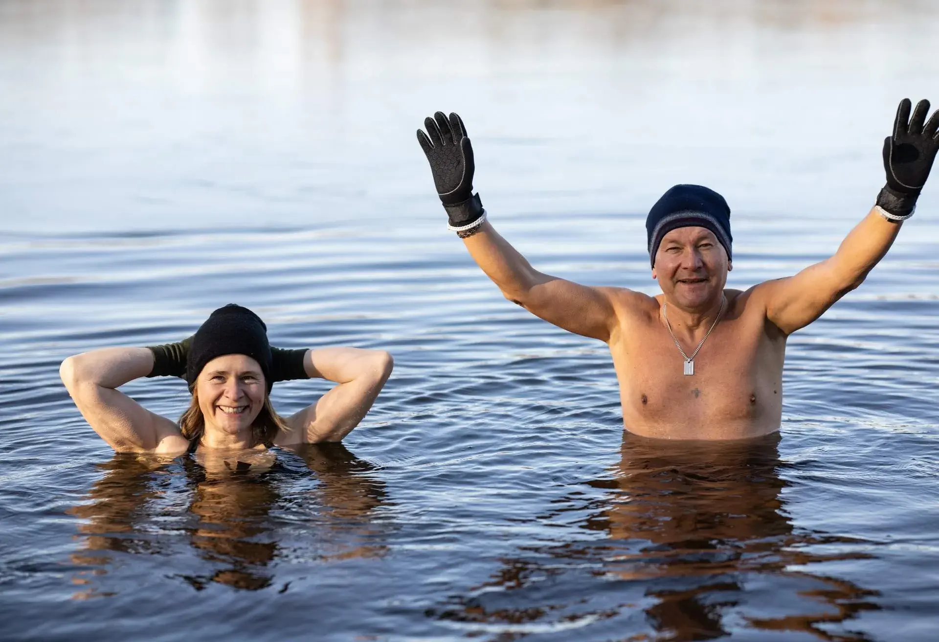 Man and woman wearing black wool hats and gloves looking at the camera during a winter swimming session