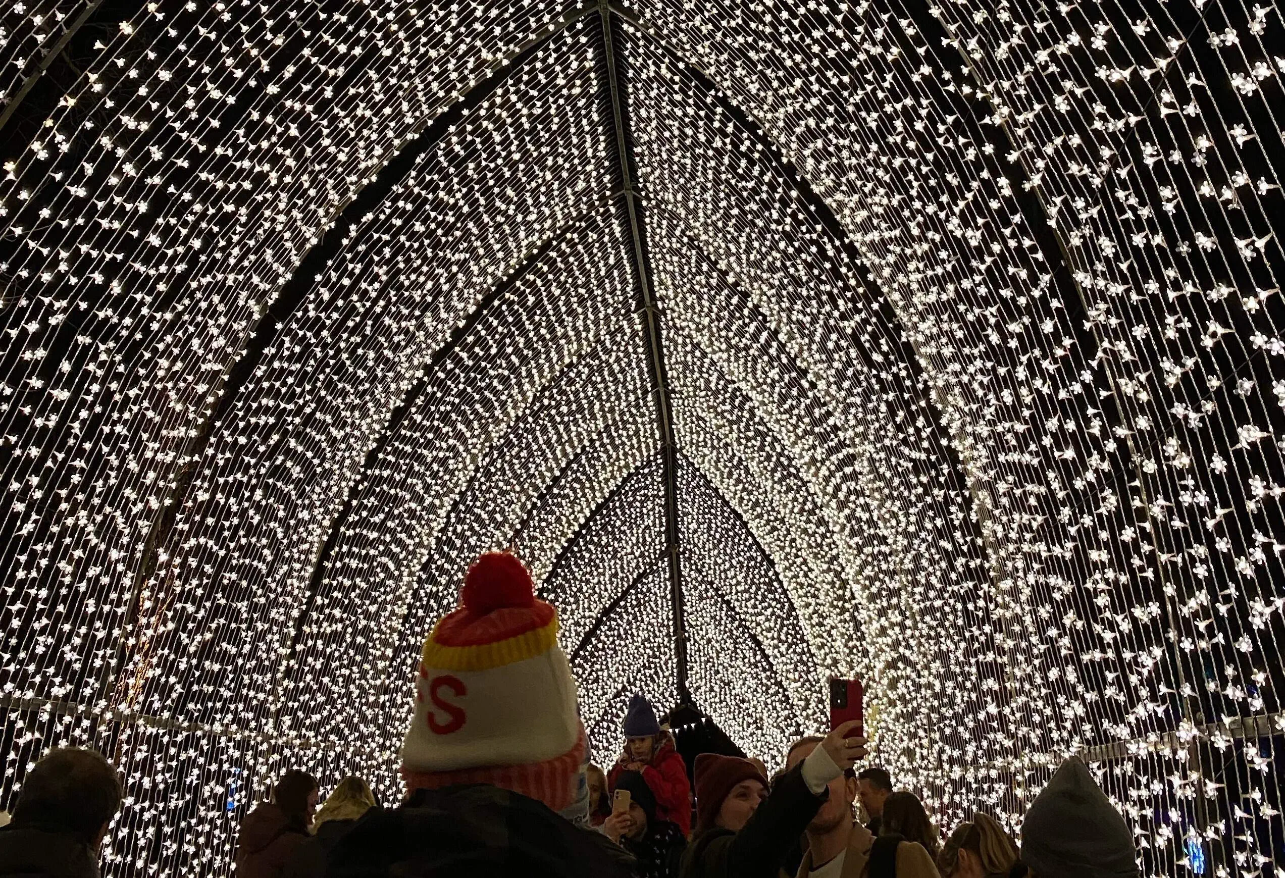 Step into a mesmerise world of festive wonder with this captivating image of a famous glittering light tunnel arched structure at Christmas at Kew, an enchanting event held in the delightful Kew Gardens, England. The sparkling lights adorn the tunnel, creating a dazzling spectacle that exudes joy and magic of the holiday season. People walk through the illuminated tunnel, some wearing bobble hats, adding a sense of merriment and excitement to the scene. This image perfectly captures the essence of Christmas cheer and the joyous ambiance of the event. Ideal for illustrating holiday celebrations, winter wonderlands, and the enchanting beauty of Kew Gardens during the most wonderful time of the year. Sparkling delights. Breathtaking display. Wonder. Joy. Festive atmosphere. Botanical gardens. Crowds of people.