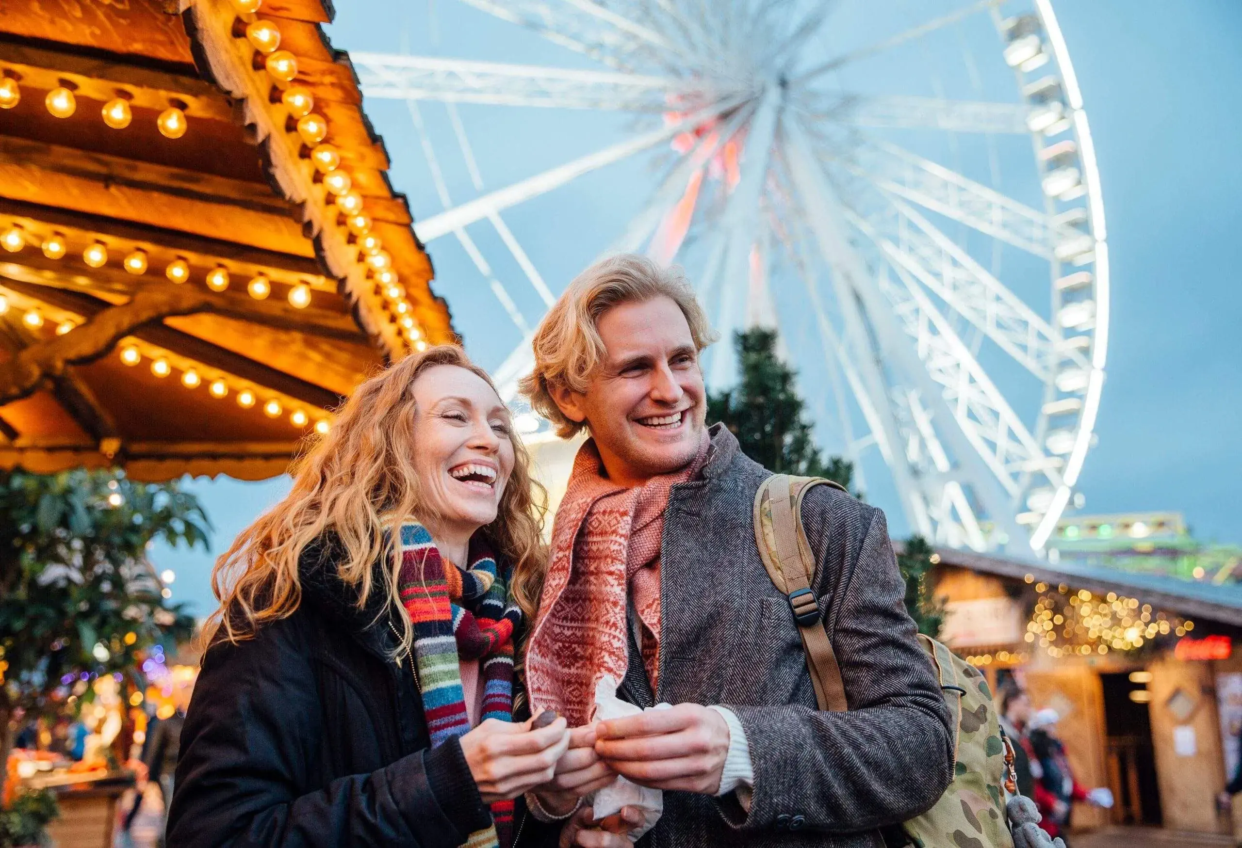 Happy couple are eating sweets and watching entertainment at the christmas fair and market.