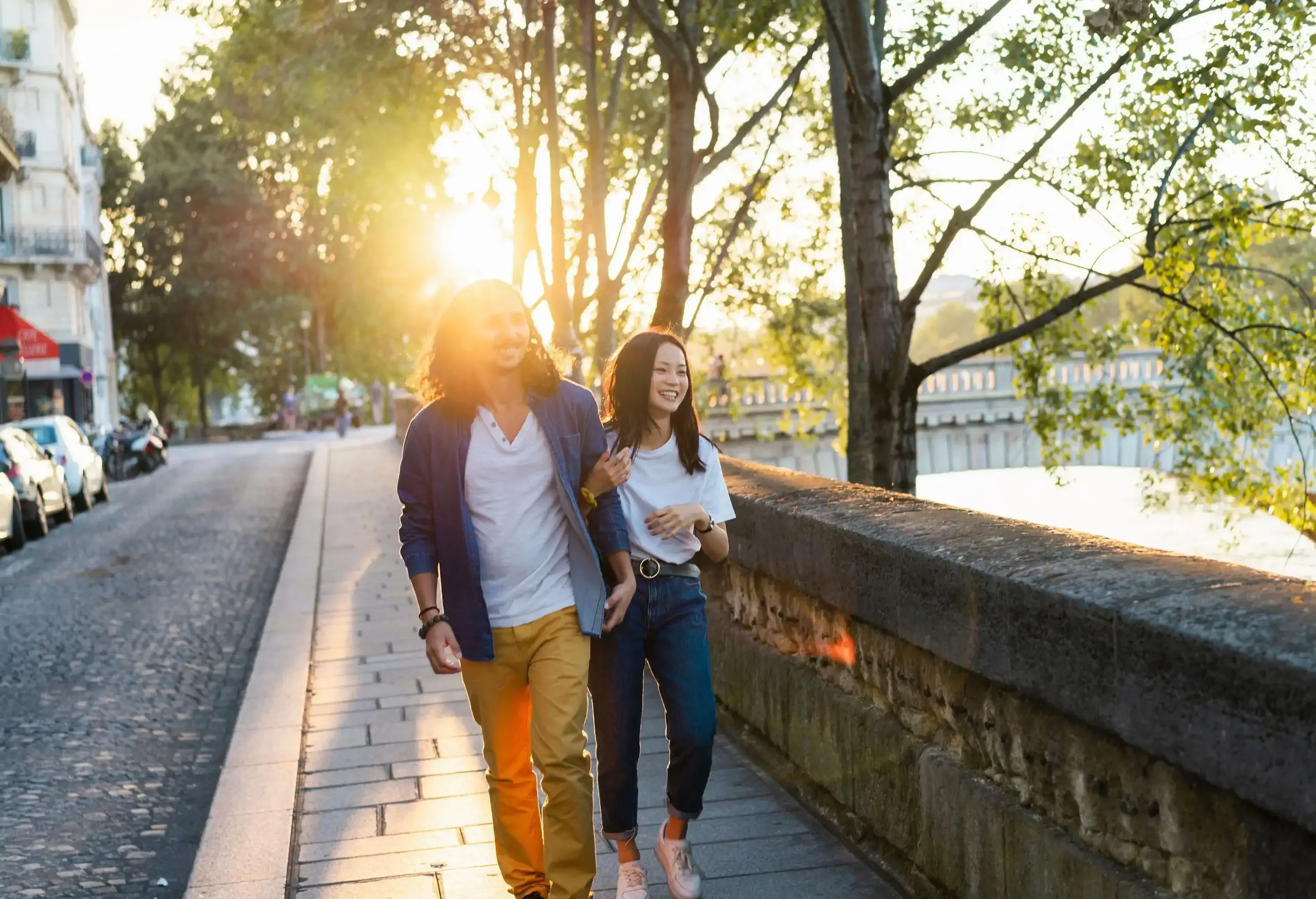 A couple strolled along the sidewalk, bathed in the warm glow of the sun peeking through the branches of the surrounding trees.