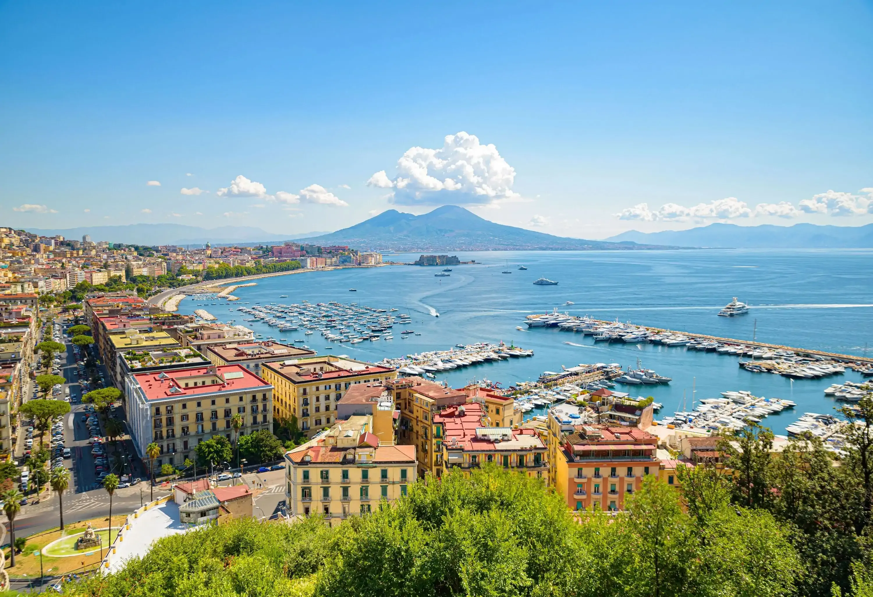 A breathtaking view of a busy harbour in a coastal town, with Mount Vesuvius visible in the distance, overlooking the sea.