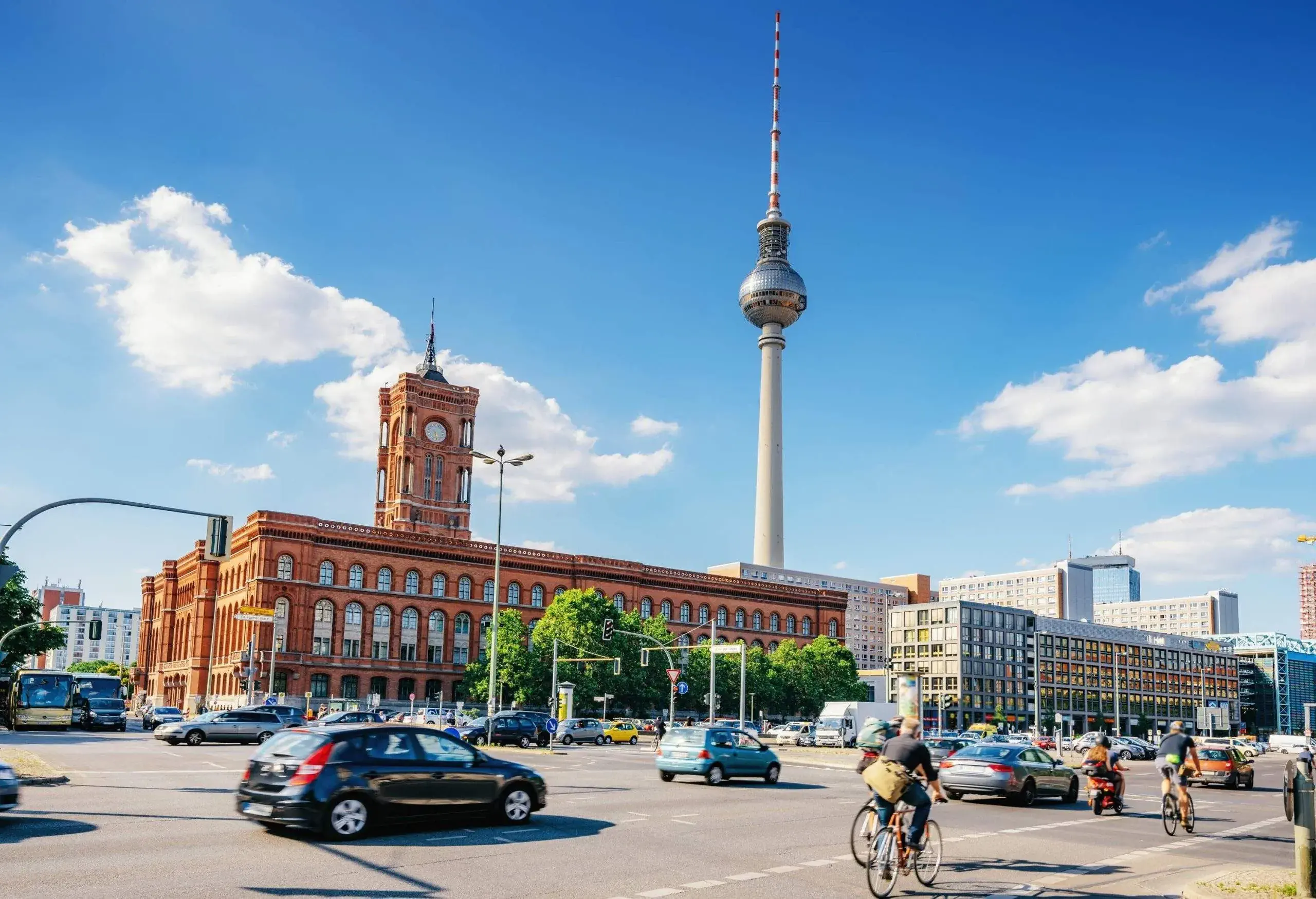 Rotes Rathaus is a red Renaissance Revival town hall with a clock tower along a bustling highway of cars and bicycles.