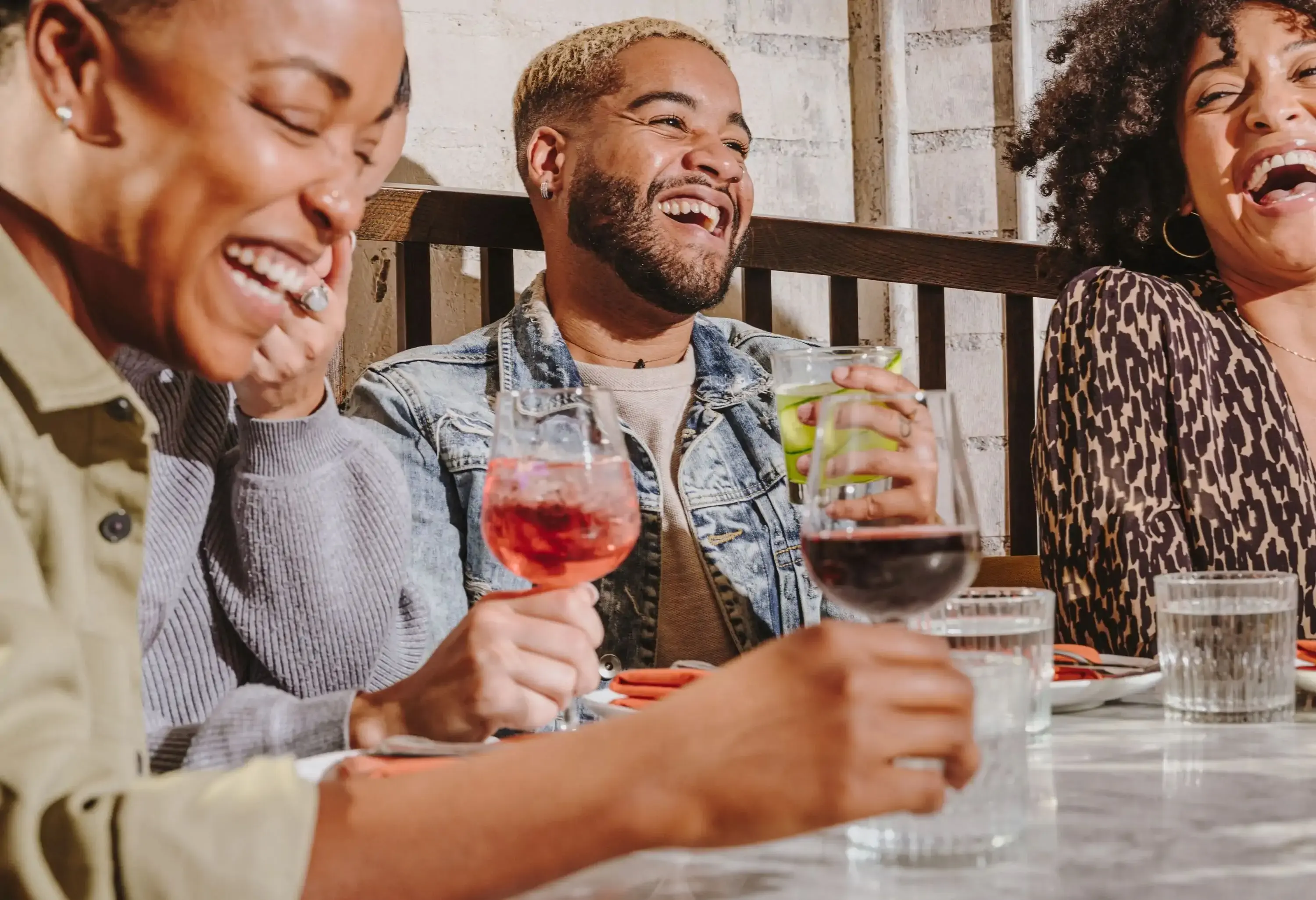 A group of four people with different types of drinks in their hands are happily conversing at a restaurant.