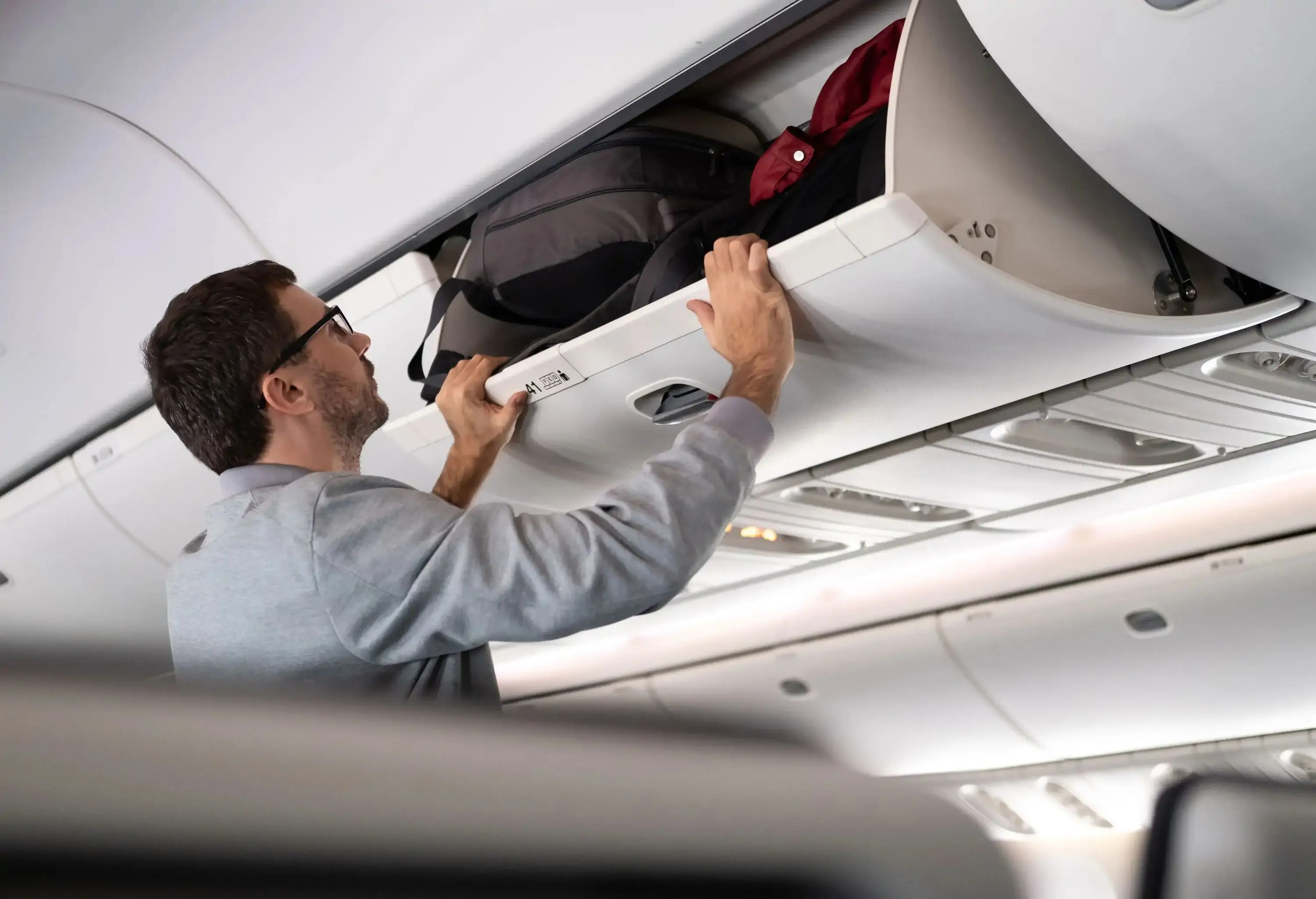 A man placing his carry-on baggage into the overhead bin