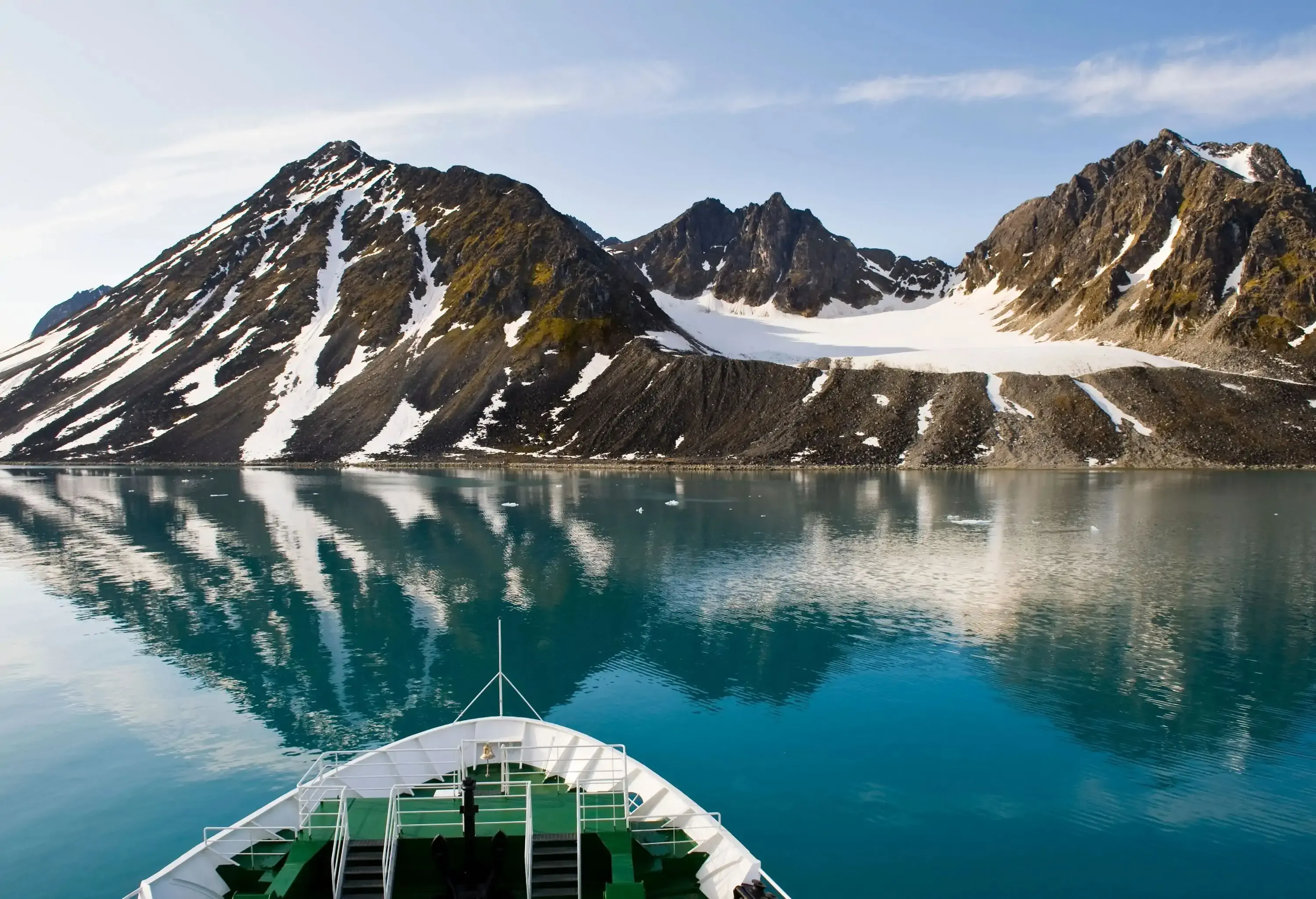 A ferry boat cruising on a wide fjord with a mirror-like surface that reflects the mountains.