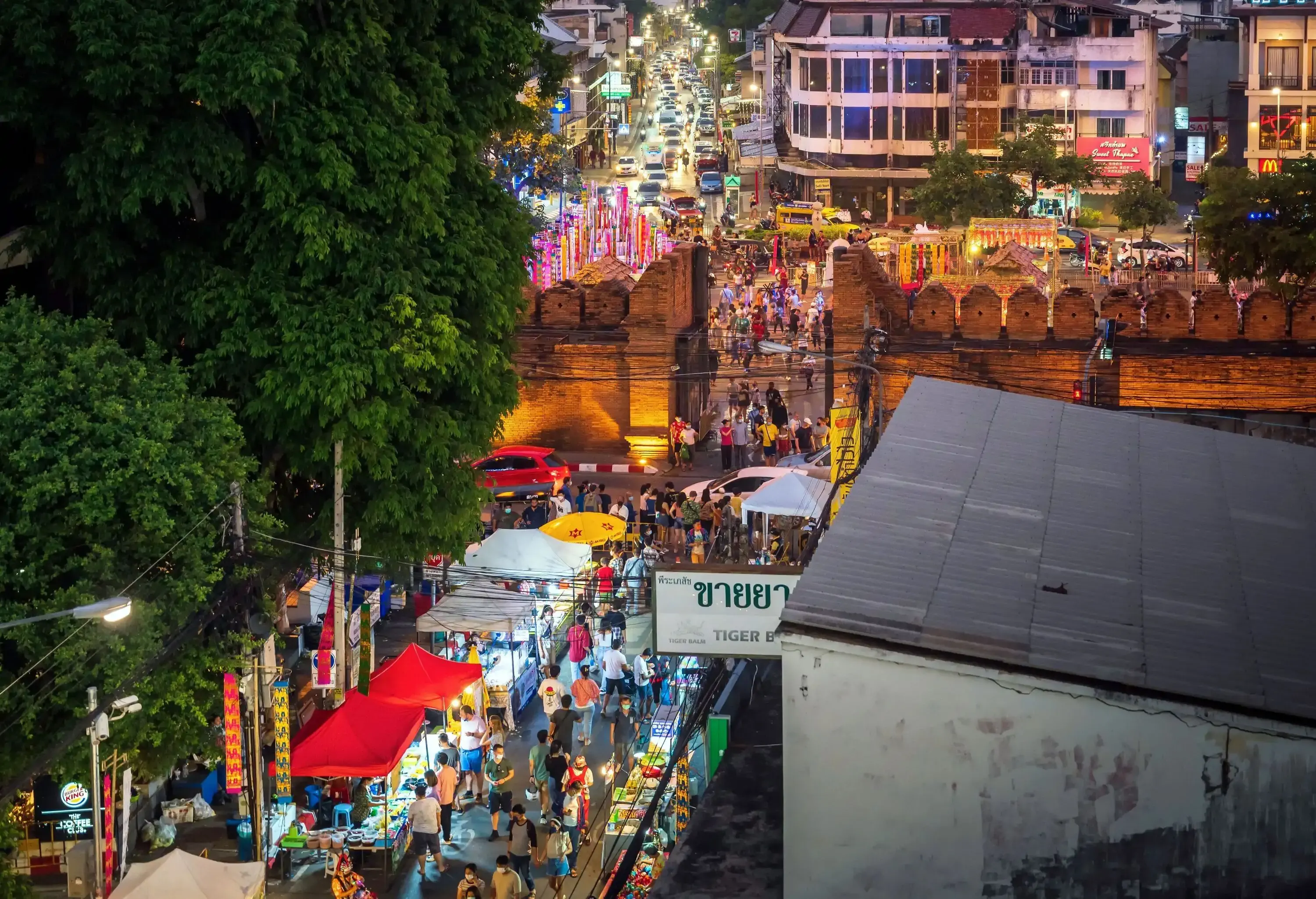 People flock to the street food market next to a bustling road at night.