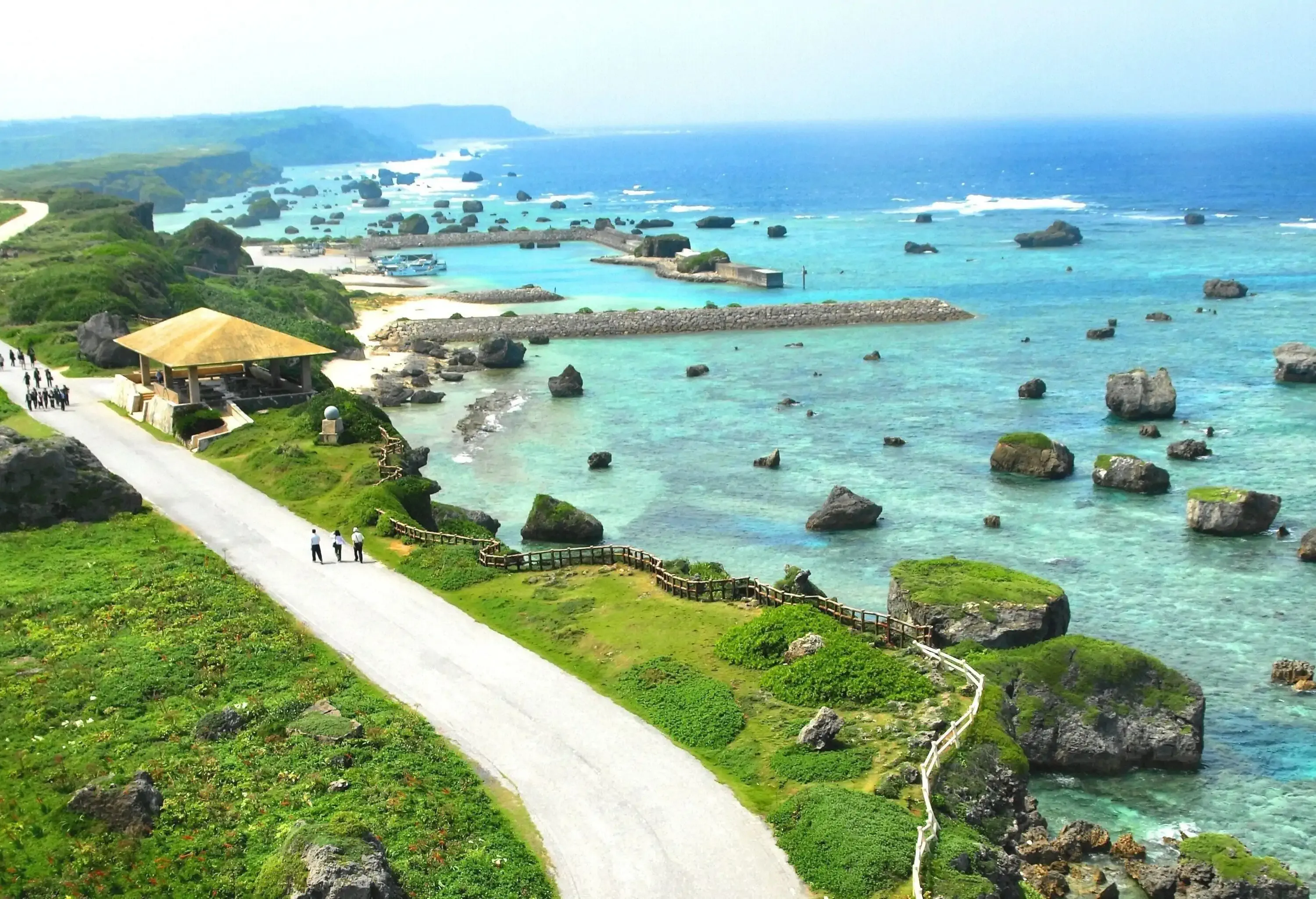 A group of tourists walk on the white promenade stretches at the tip of the cape with a fantastic view of the vast blue ocean.