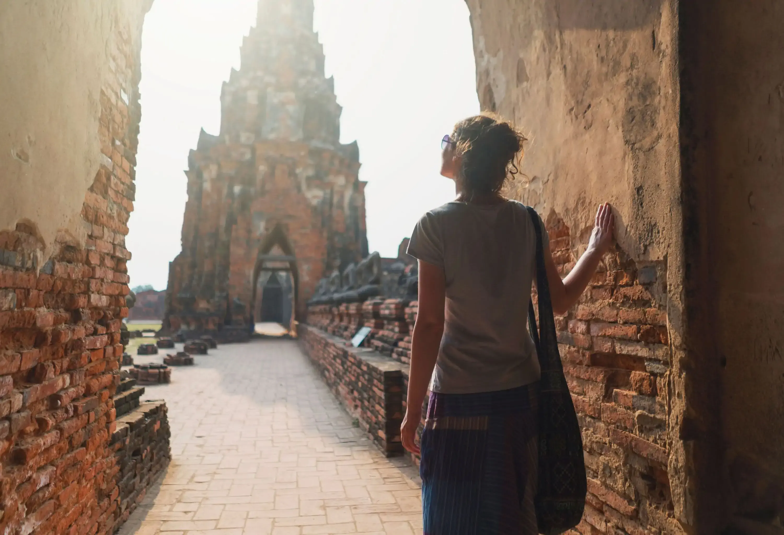 A tourist in casual clothes touches the damaged walls of a brick temple.