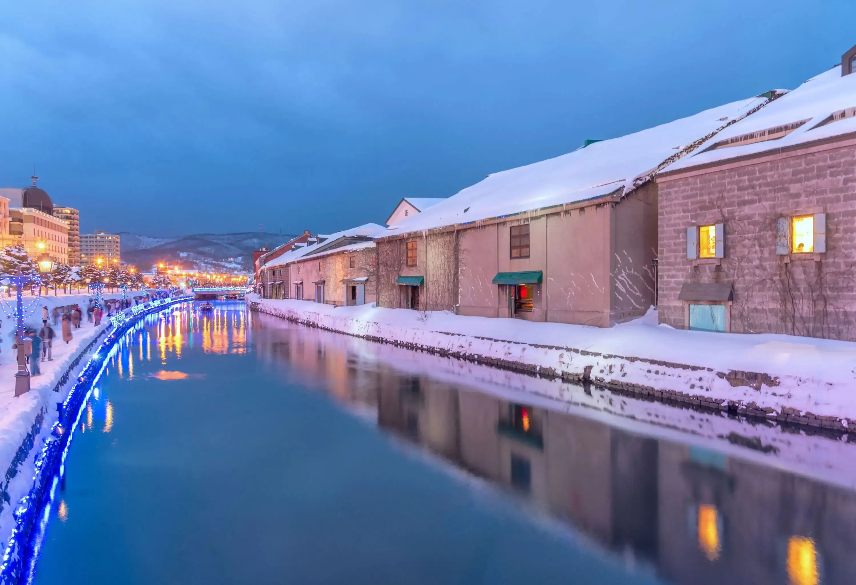 A calm water canal lined with blue LED lights along a crowded promenade covered in snow.