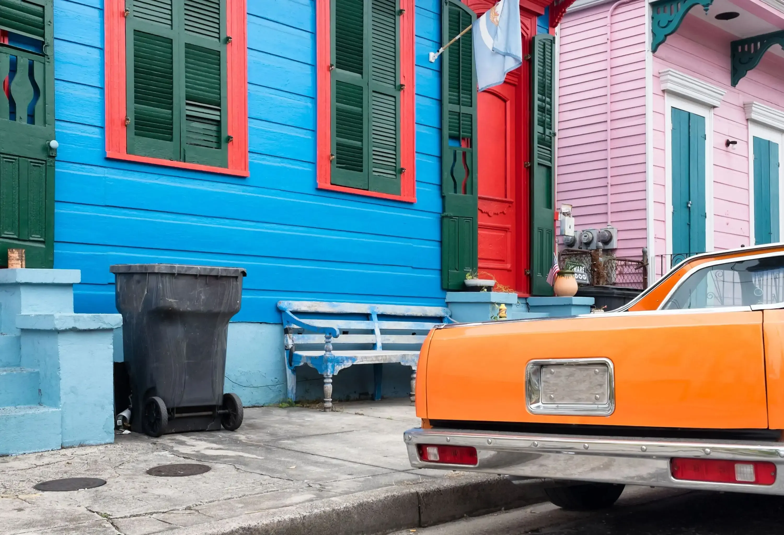 Colourful, vintage-painted houses are complemented by a classic orange car parked in front, capturing the essence of timeless charm.