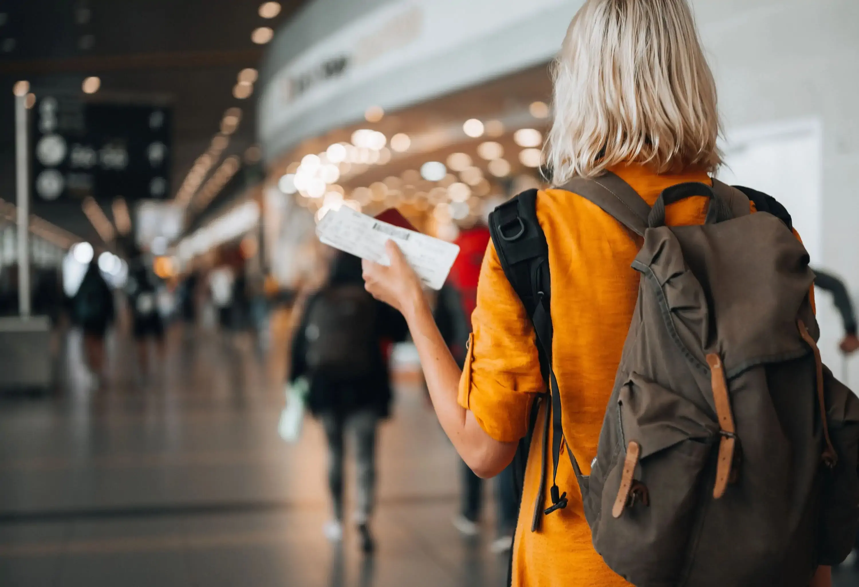 Rear view of a  woman at the airport holding a passport with a boarding pass as she walks to her departure gate