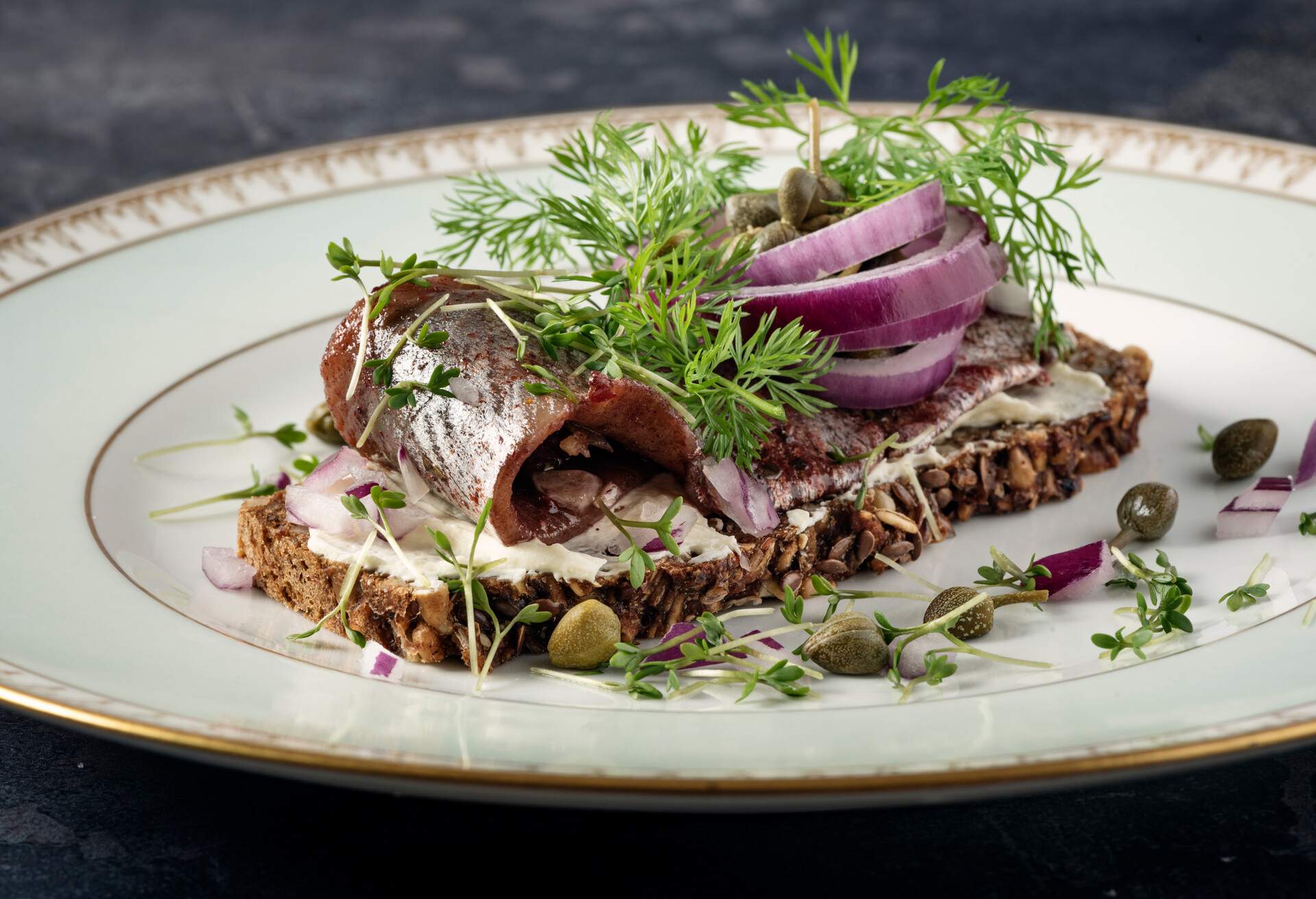 Traditional danish “smørrebrød” or open sandwich made with a slice of buttered rye bread, marinated herring, shavings of horseradish and topped with red onion, fresh dill and capers. Colour, horizontal format with some copy space. Smorrebrod are a staple of the danish food culture, a very popular choice for lunch or a light dinner. Toppings can be almost anything from roast beef to prawns but the rye bread at the bottom of the sandwich has to be good!