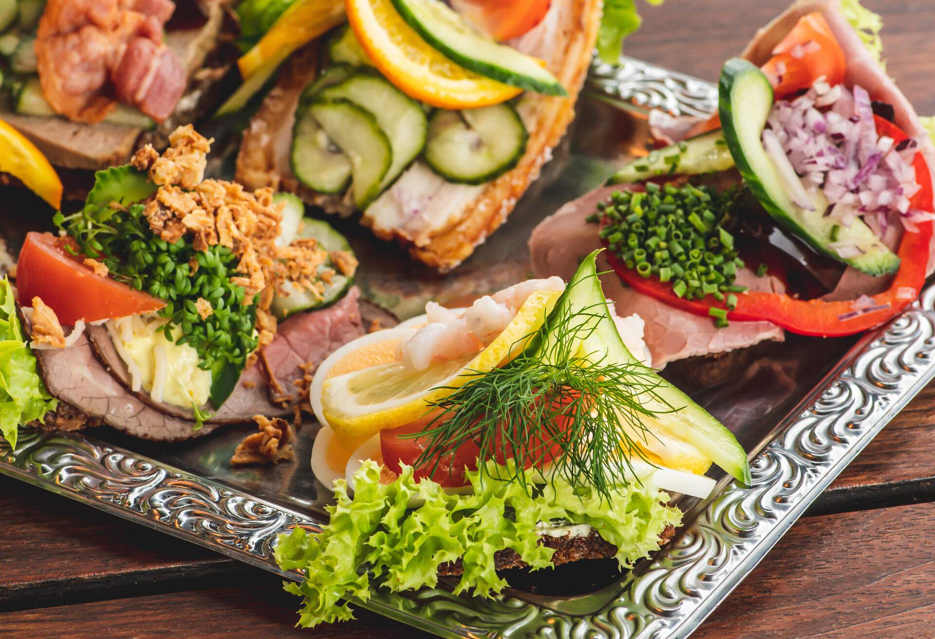 Danish traditional Smørrebrød or open sandwiches served in a plate, roast beef with remoulade, tomato and shredded horseradish on Danish rye bread, egg, prawns, lemon and mayonnaise