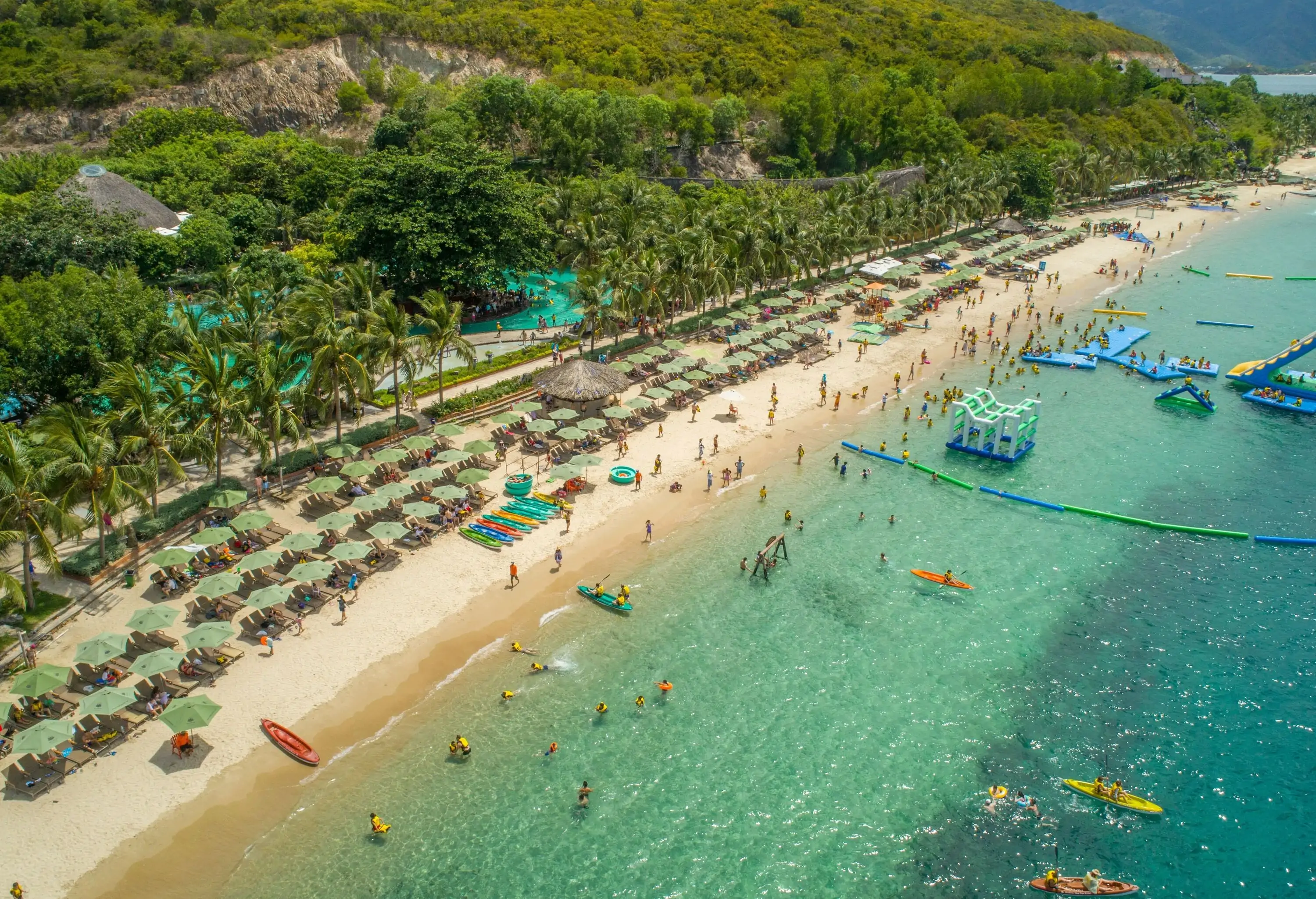 A beach resort featuring a floating playground in clear waters and umbrellas on the sand.