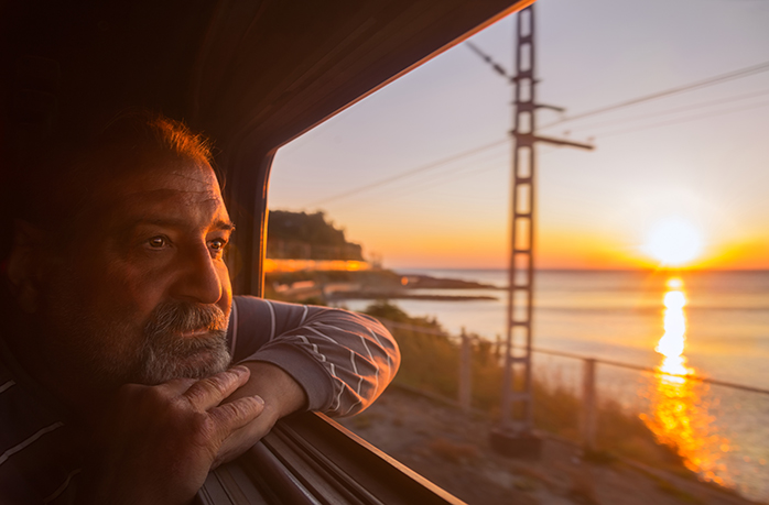 Elderly man admires sunset over the sea from open window of train