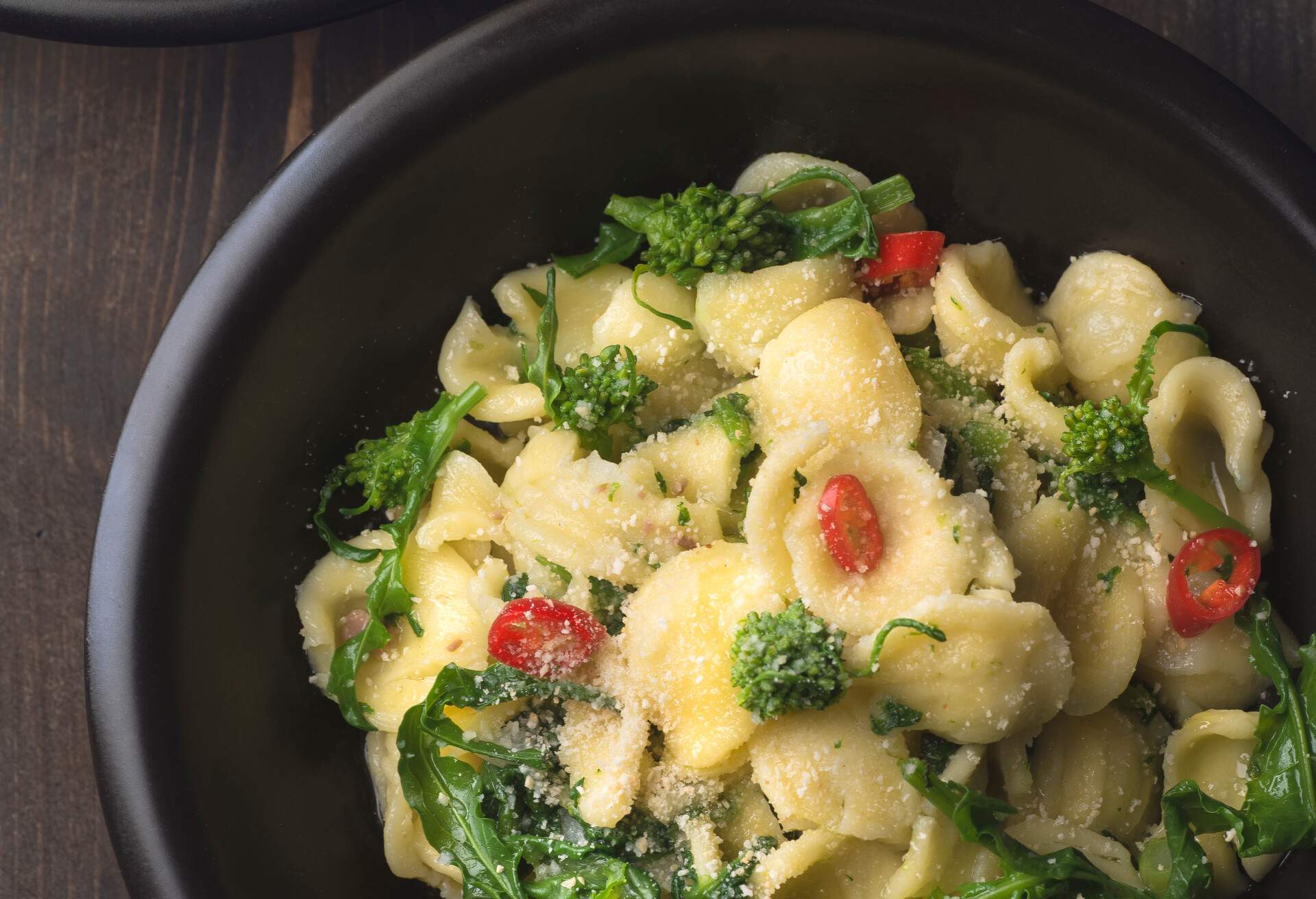 Italian pasta Orecchiette with turnip leaves (cima di rapa) and tops with garlic, hot pepper, grated bread on a dark wooden background. Recipes of southern Italy, Puglia. Poor cuisine or cuisine of simple ingredients, close up