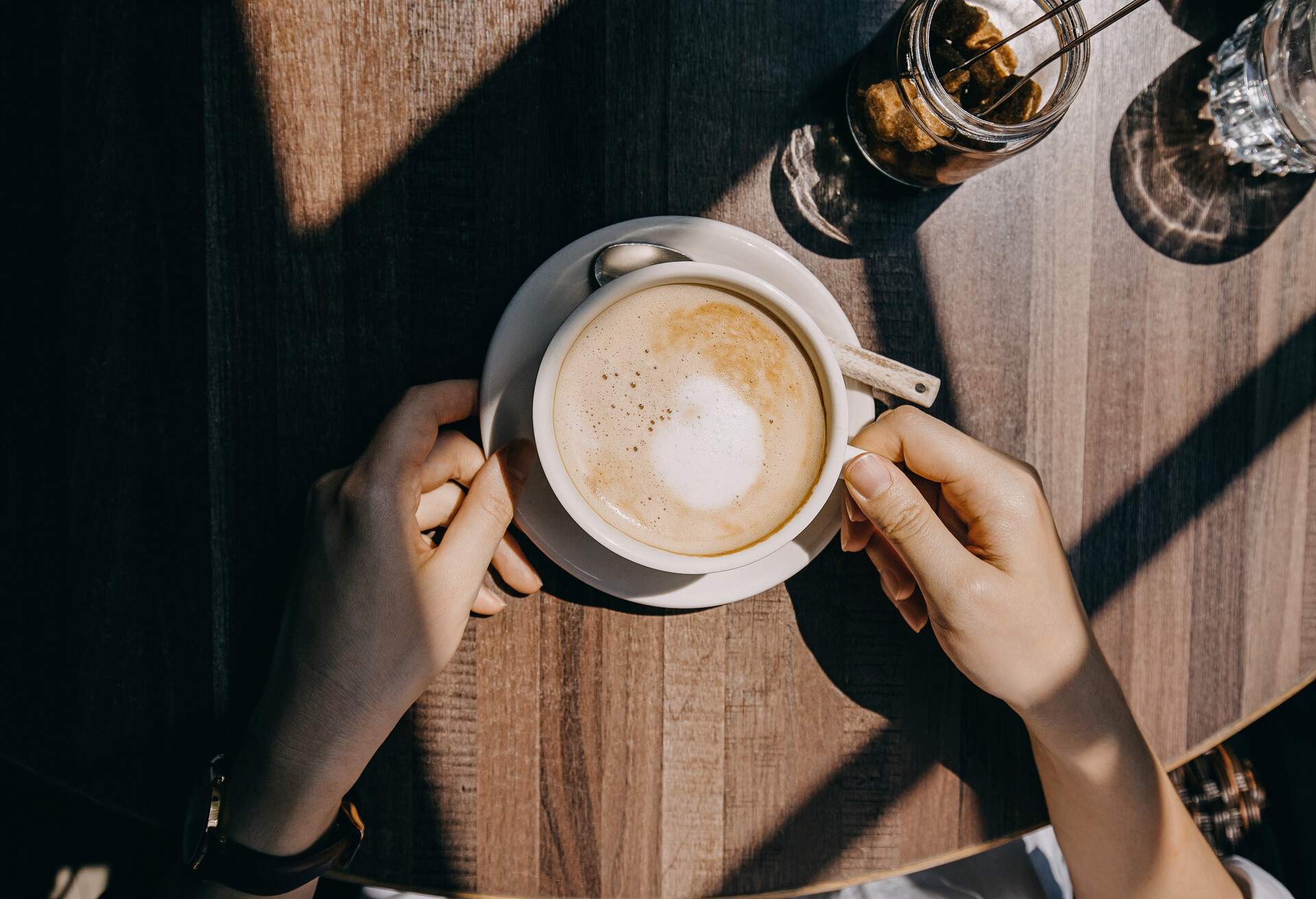 Top view of woman sitting by the window in coffee shop enjoying the warmth of sunlight and drinking coffee