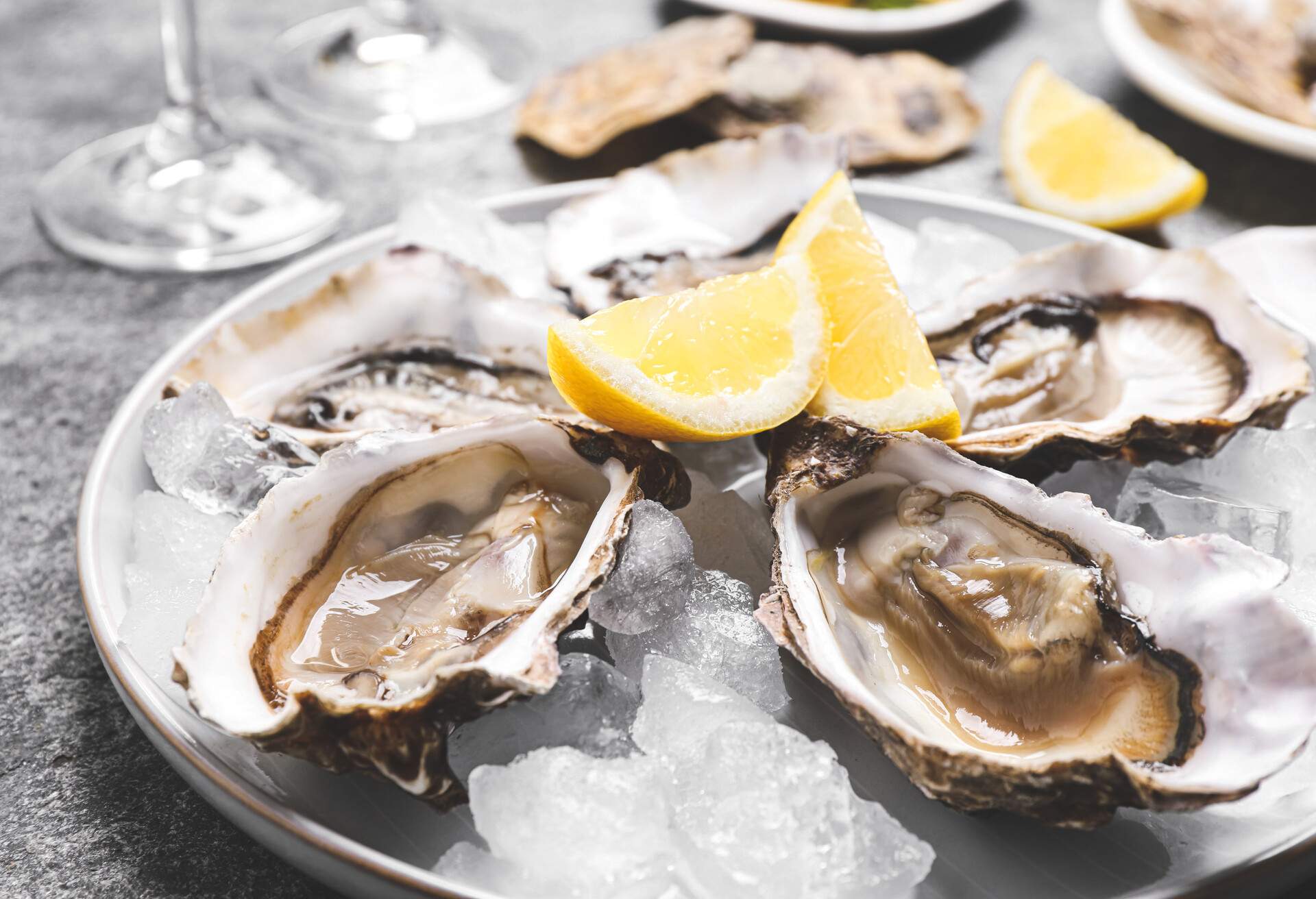 Fresh oysters with lemon and ice on grey table, closeup