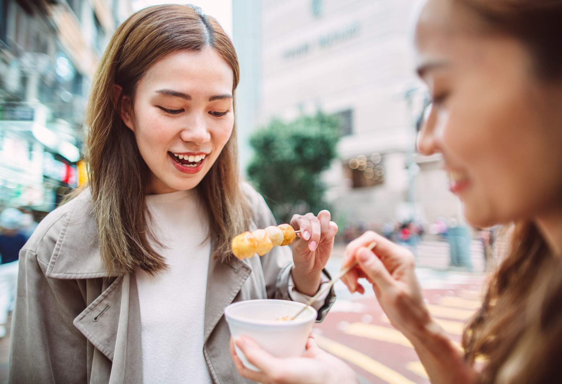 Two young pretty women enjoying Hong Kong local street food fish balls joyfully