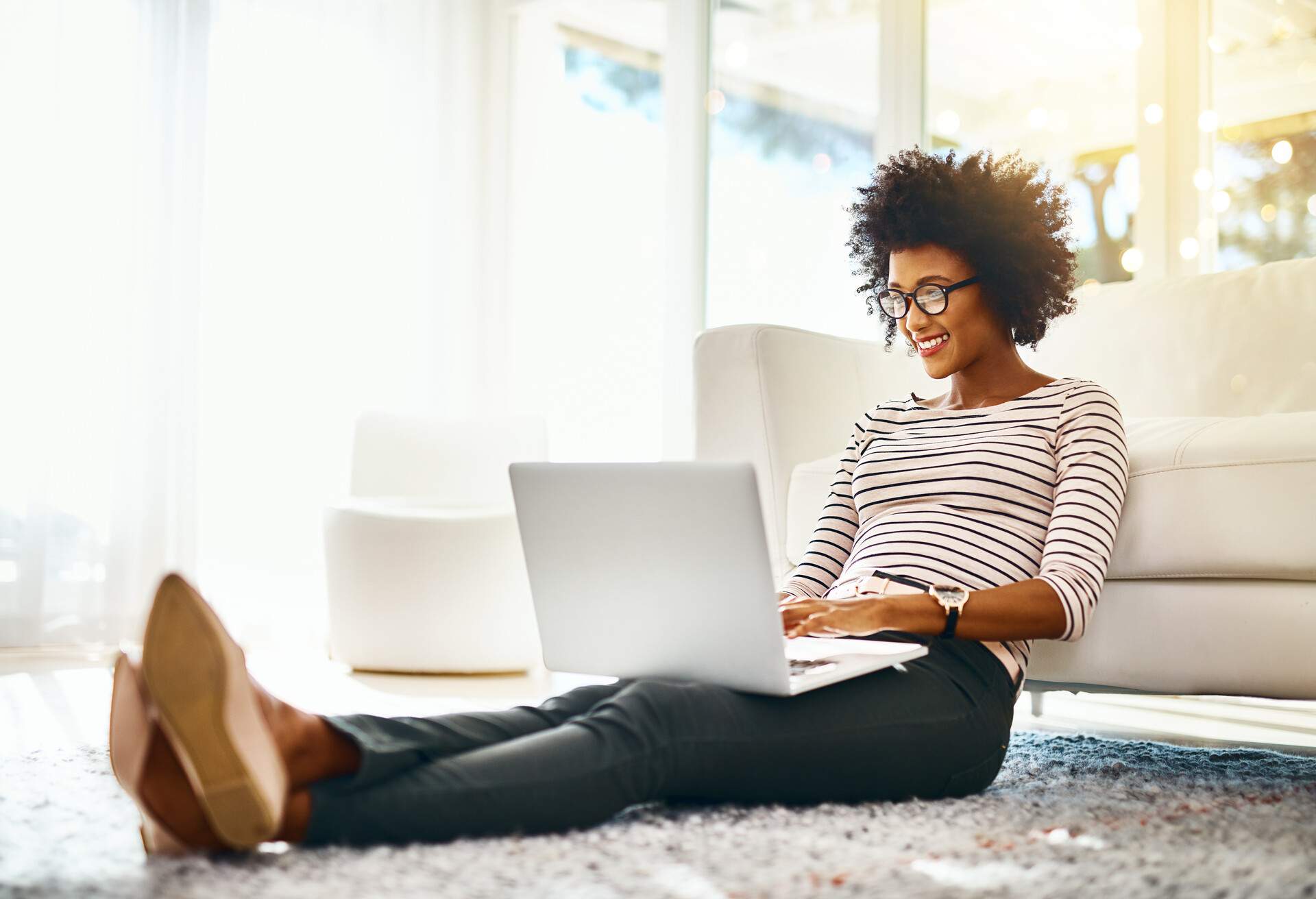 Shot of a cheerful young woman doing online shopping on her laptop while being seated on the floor at home