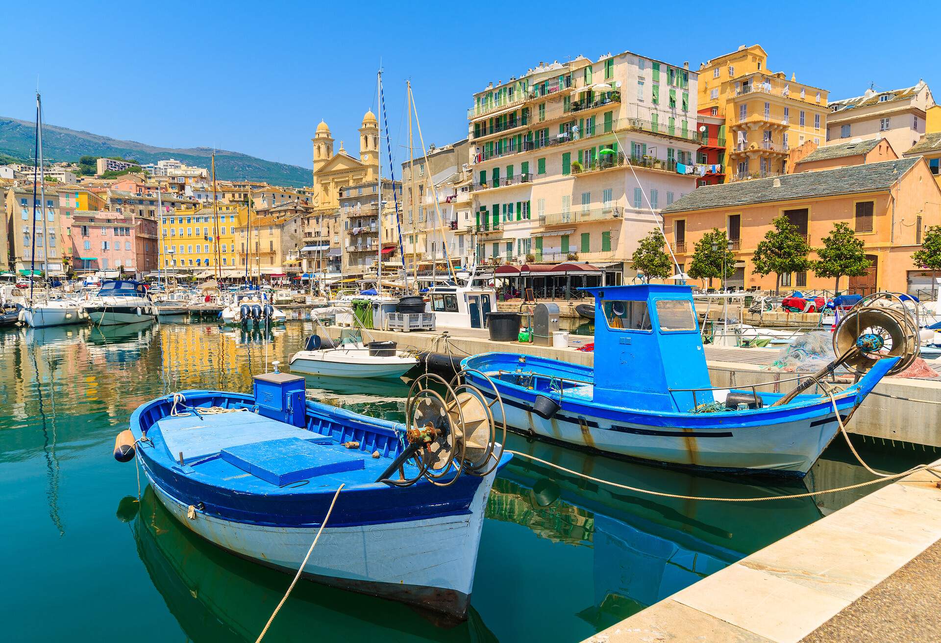 Fishing boats moored in a harbour across from the colourful buildings along the coast.