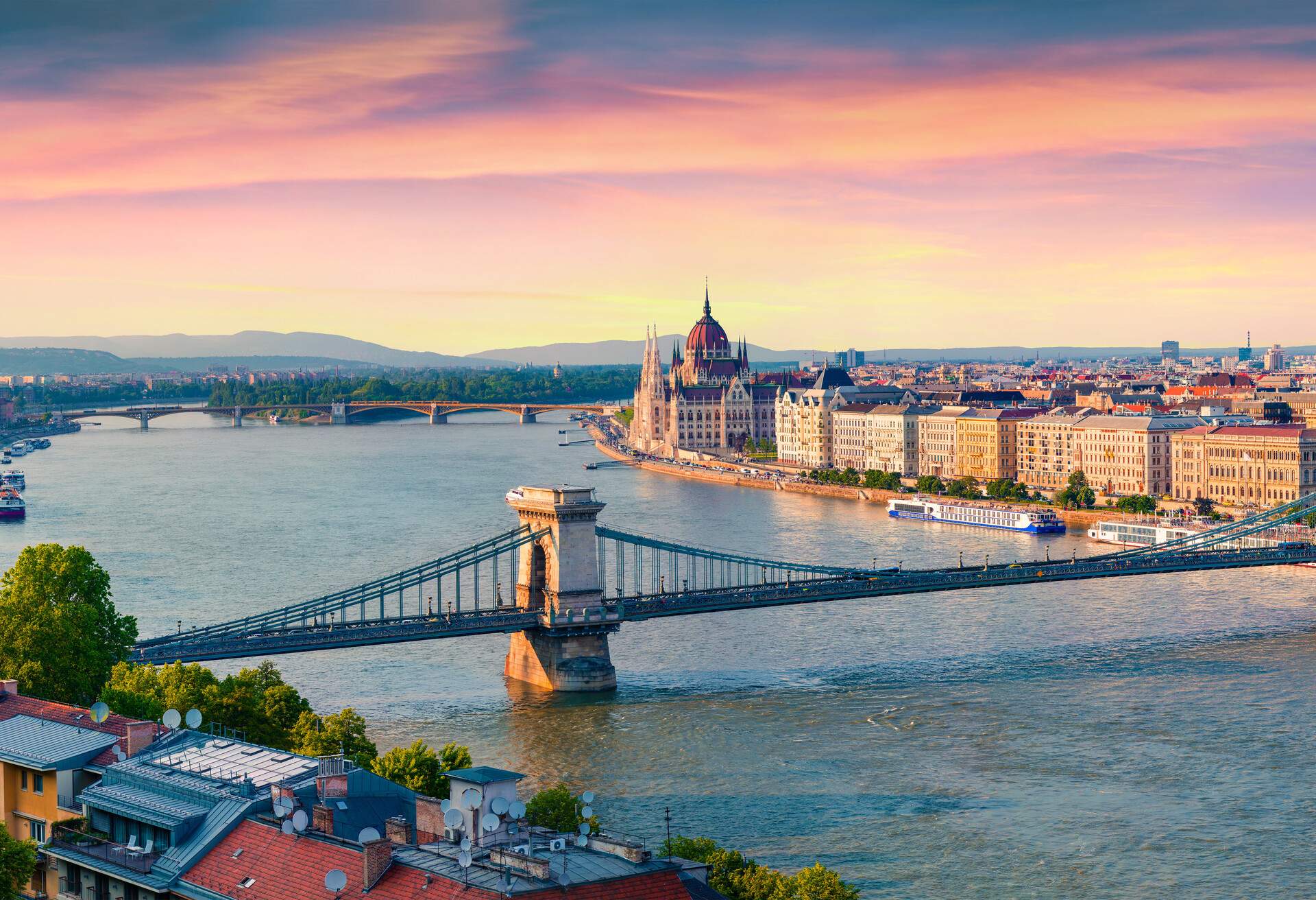 A suspension bridge across a river with views of a cityscape.