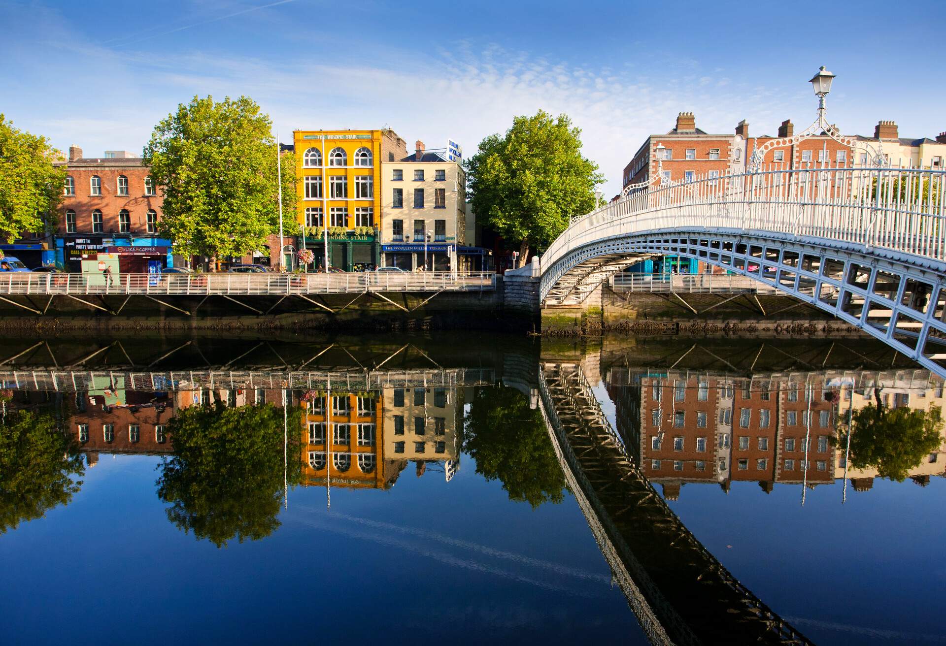 A peaceful river reflects the nearby row of homes across an arch bridge.