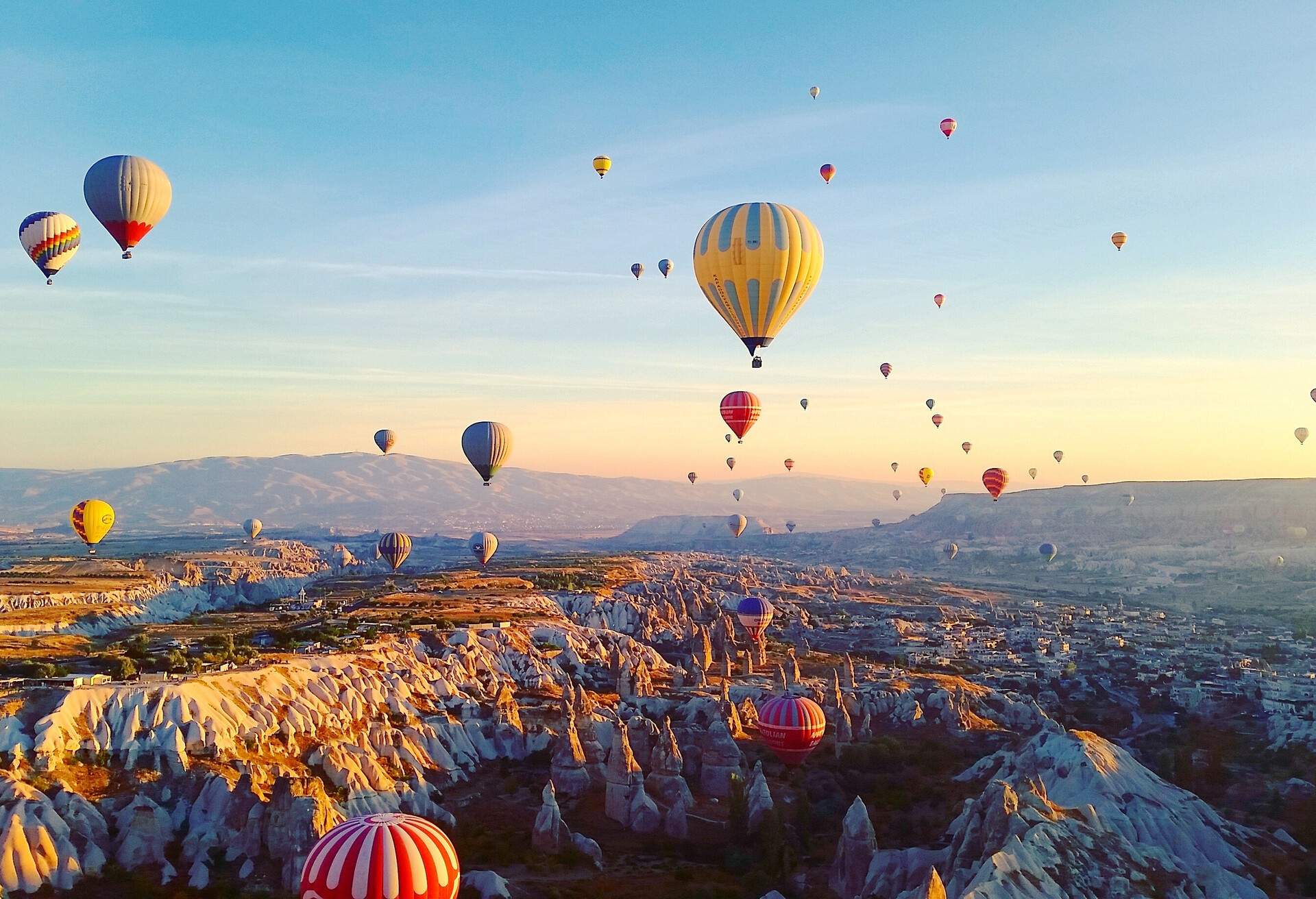 Numerous multi-coloured hot air balloons fly above a vast valley of spectacular weaving rock formations.