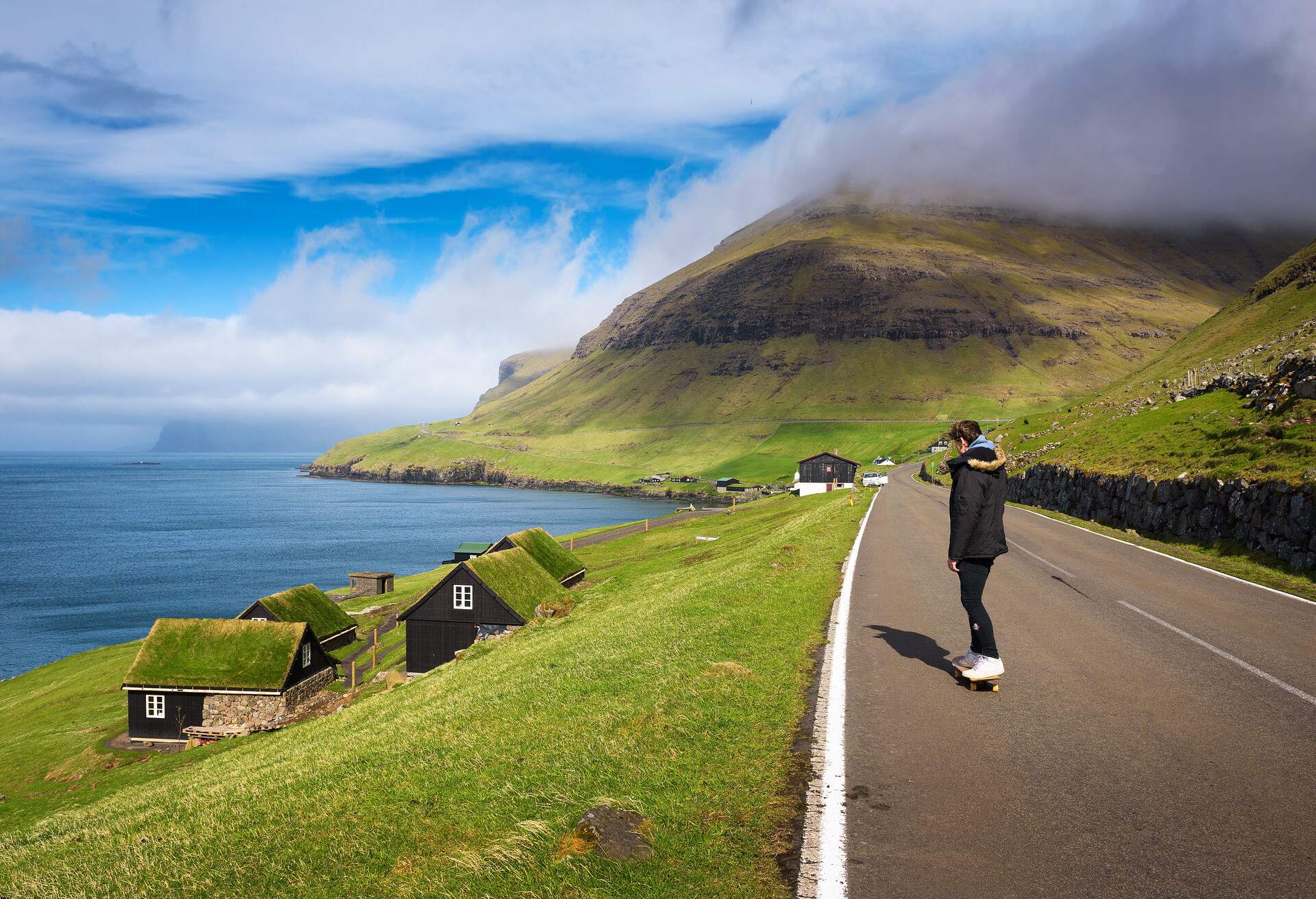 Skater riding a skateboard through the coastal village of Bour on the Faroe Islands