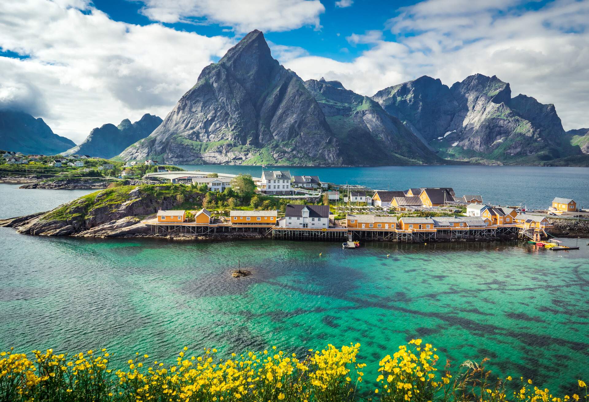 Beautiful summer landscape panorama with yellow wooden traditional houses on the sea near mountain range in background, Lofoten Islands, Norway