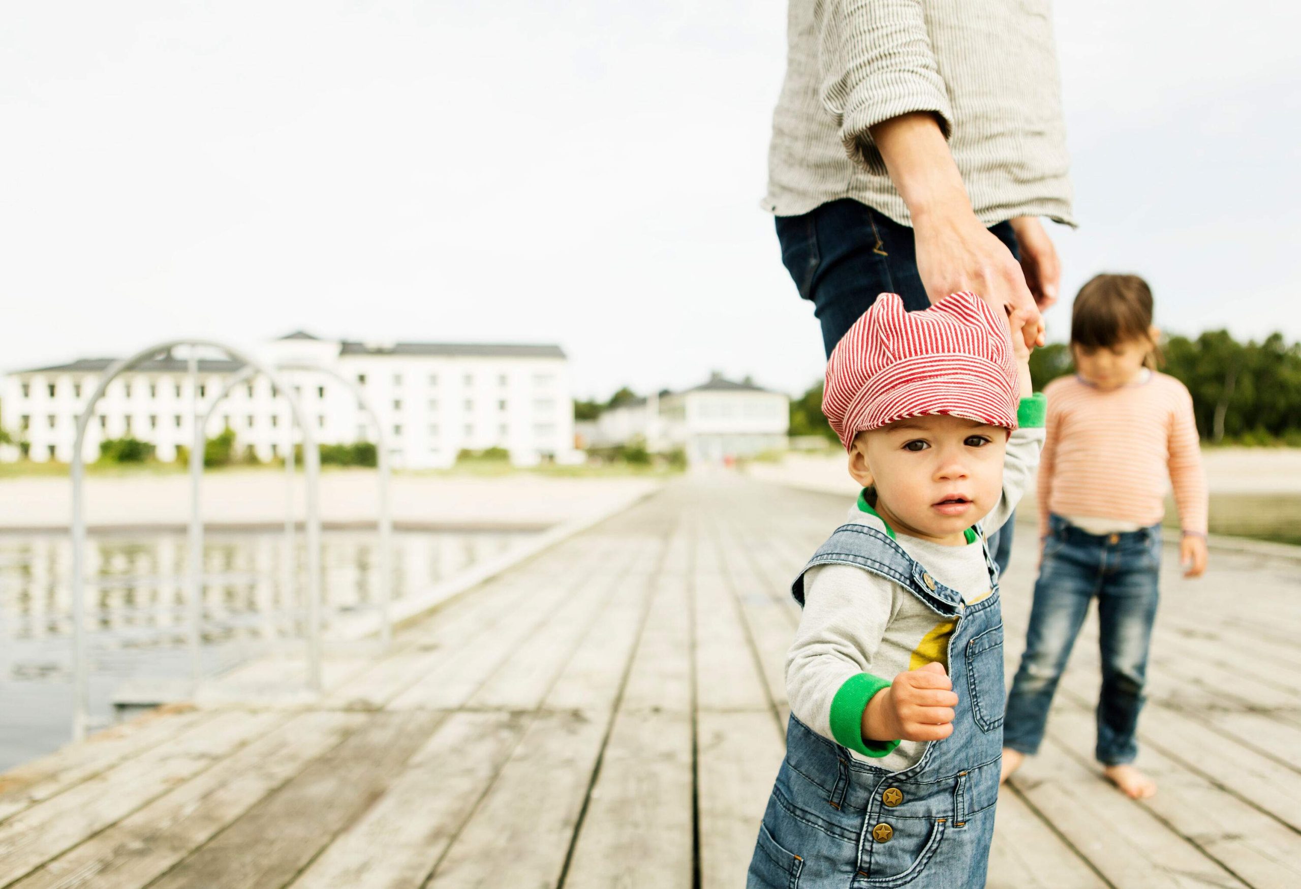 An adult person and two small children standing on a wooden pier.