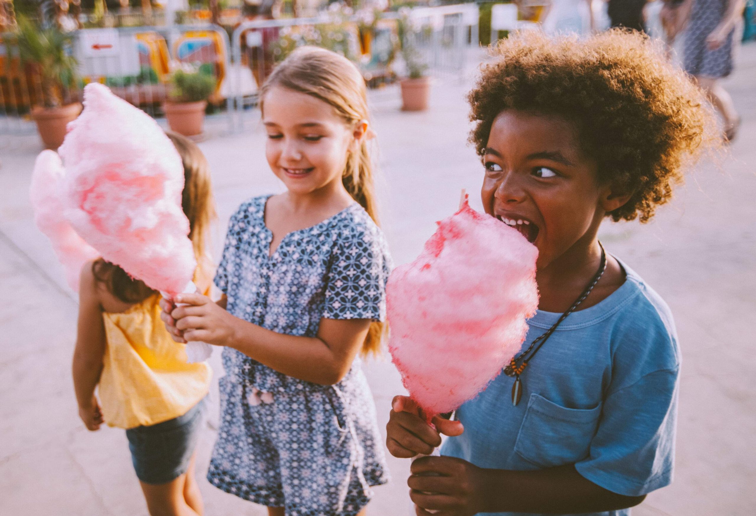 Delighted children with beaming smiles tuck into fluffy pink cotton candy, their faces lighting up with joy as they relish the sweet treat.