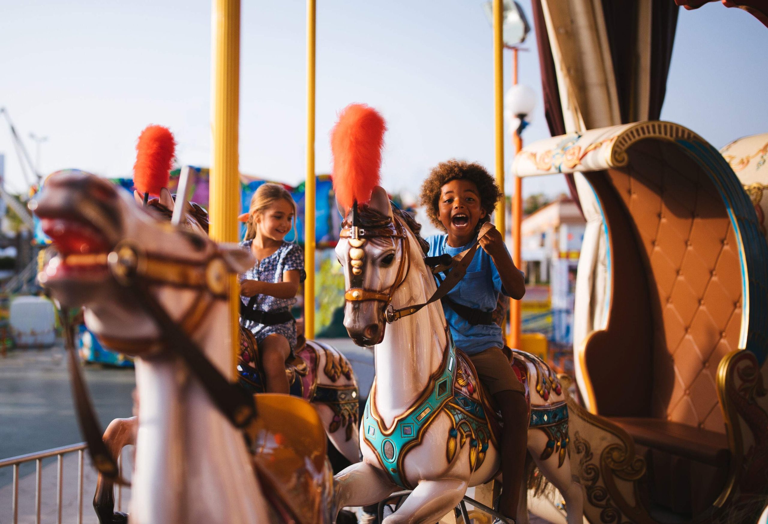 Two kids enjoy riding colourful horse mounts in a carousel.